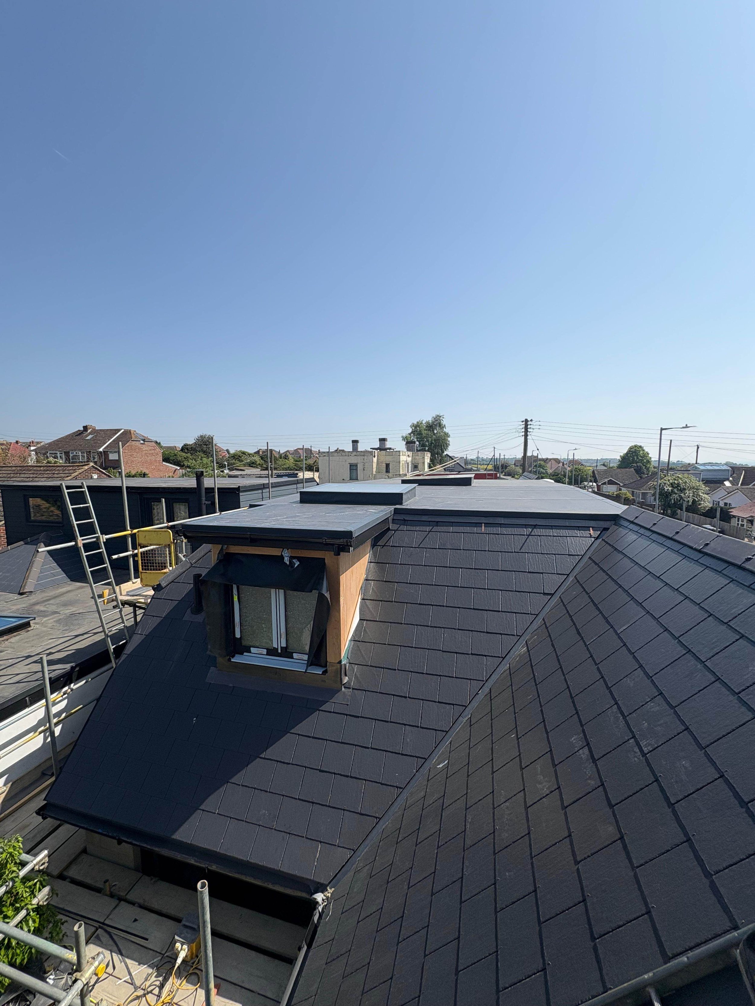 View of a residential rooftop with black shingles, a dormer window, and a clear blue sky.