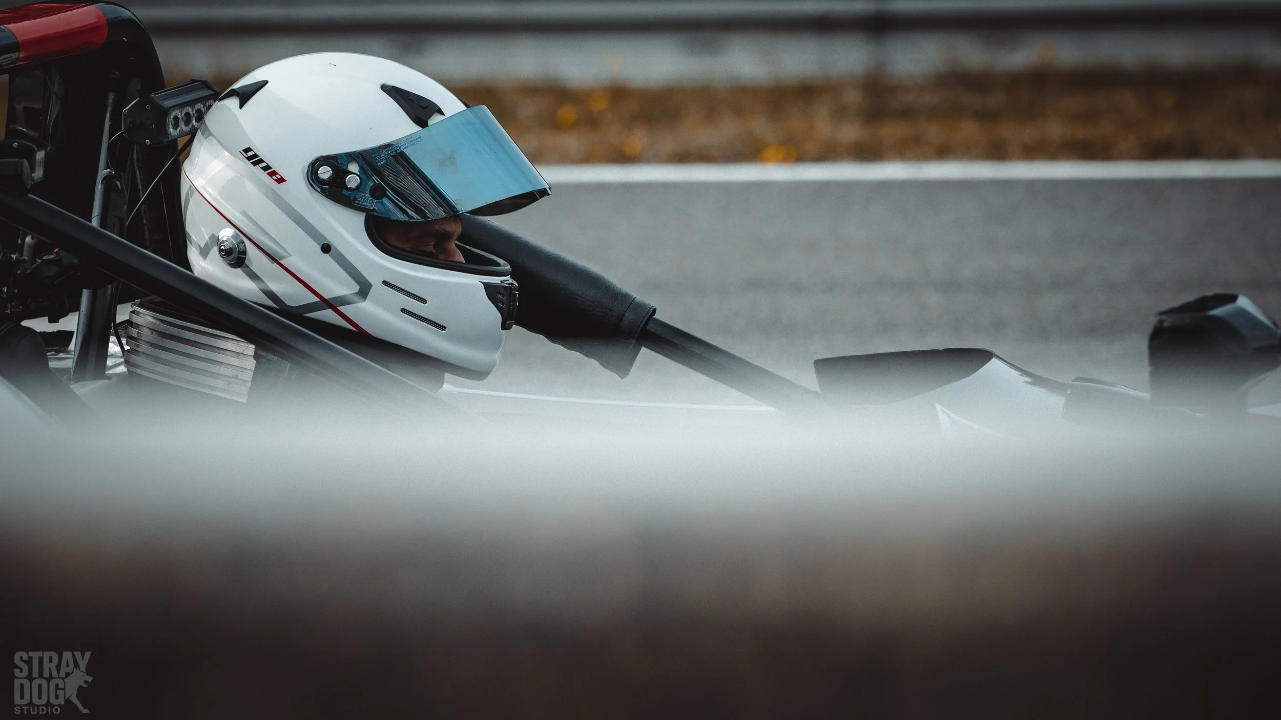Close-up of a person wearing a white racing helmet inside a race car on a track.