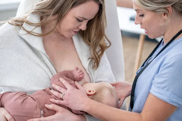 Eine Frau stillt ihr Baby, während eine Krankenschwester zuschaut.