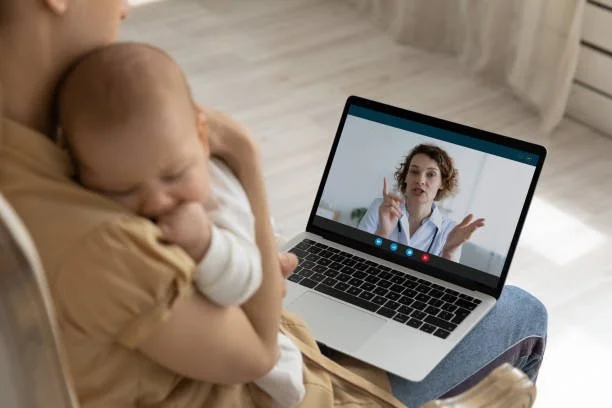 Ein Baby wird auf dem Schoß einer Mutter gehalten, während sie einen Videoanruf auf einem Laptop führt.