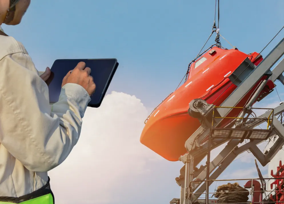 A person in a white jacket is using a tablet at a construction site near an orange helicopter or rescue vehicle hanging from a crane.