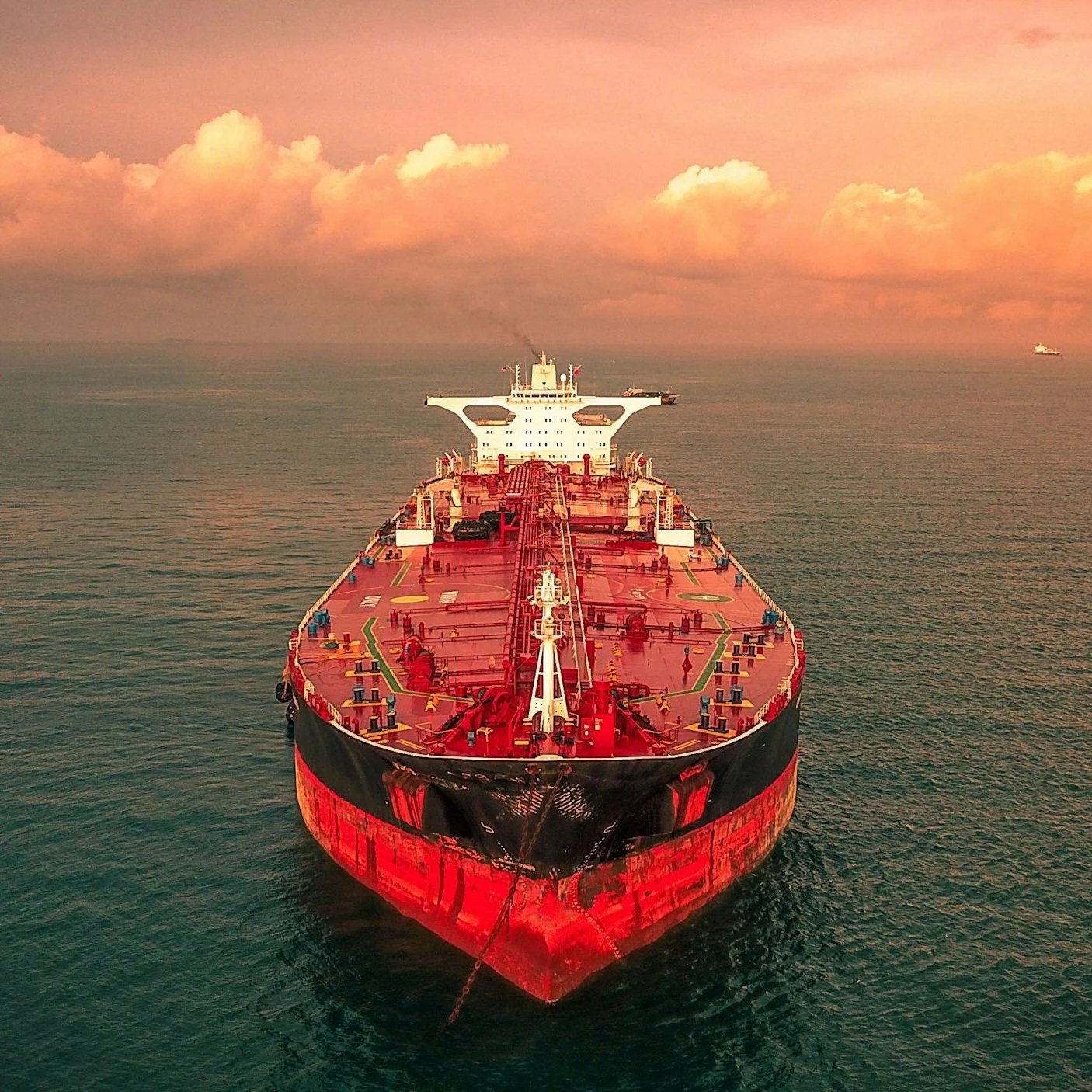 A large oil tanker ship at sea during sunset or sunrise, with a pinkish and orange sky and clouds in the background.
