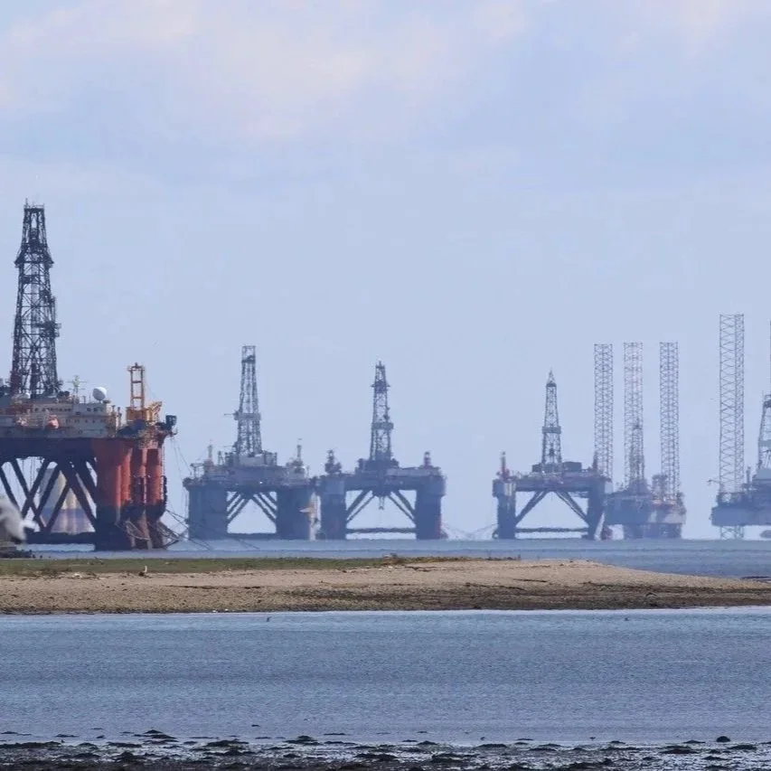 Multiple oil drilling platforms off the coast with some land in the foreground