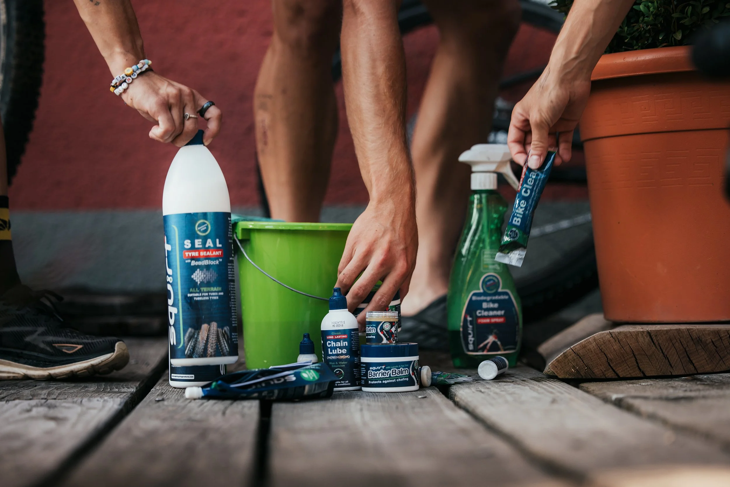 Personne effectuant la maintenance d'un vélo avec des produits de nettoyage, de lubrification et de réparation posés sur un plancher en bois.