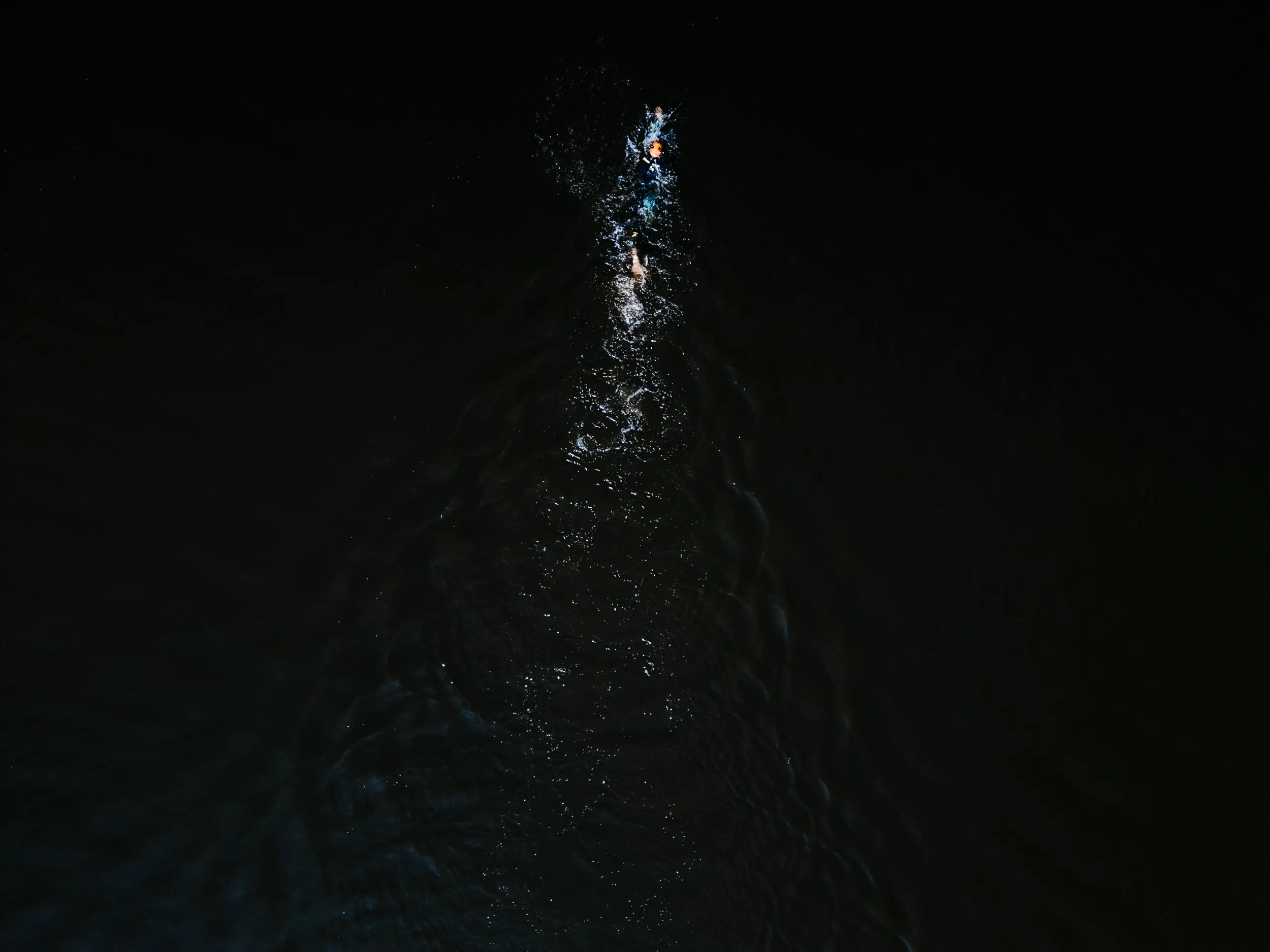 Une personne nage dans une rivière ou un lac noir, vue du dessus, avec de l'eau éclaboussée à la surface.