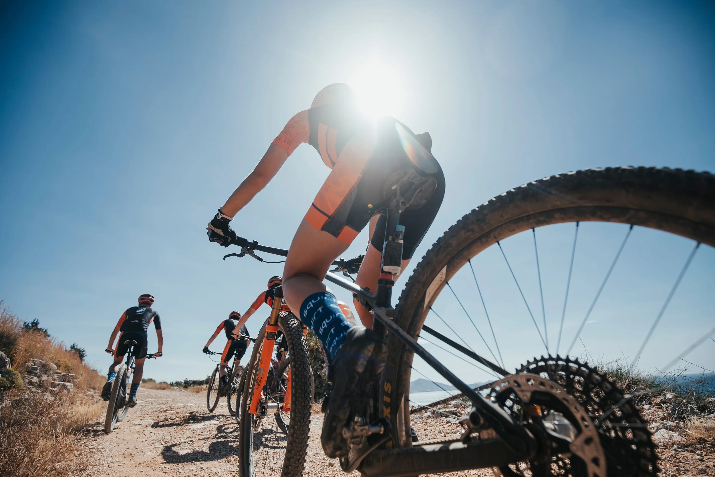 Un groupe de cyclistes en VTT roulant sur un sentier ensoleillé, avec le soleil haut dans le ciel.