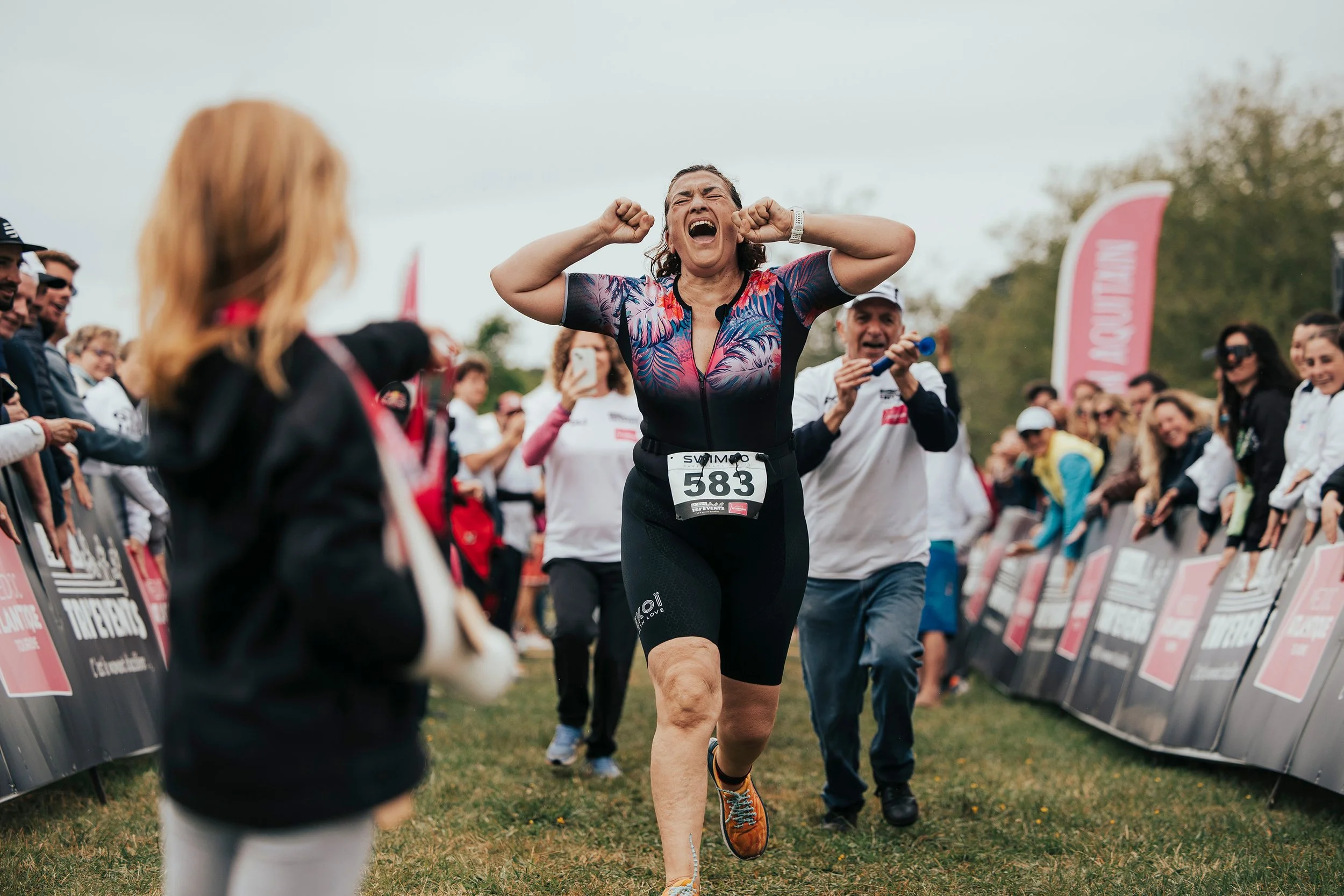 Une femme courante en pleine course, célébrant sa victoire, entourée de supporters et de spectateurs, lors d'une course en plein air.