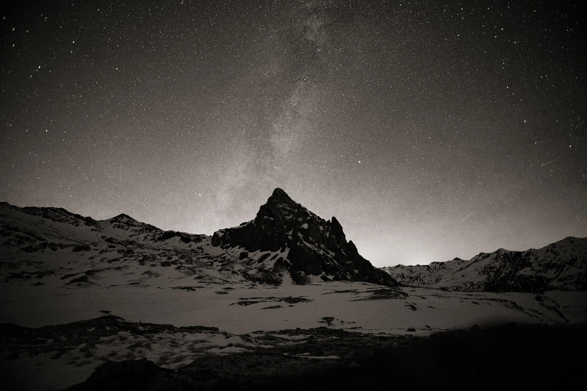 Montagne enneigée sous un ciel étoilé, en noir et blanc. La voie lactée.