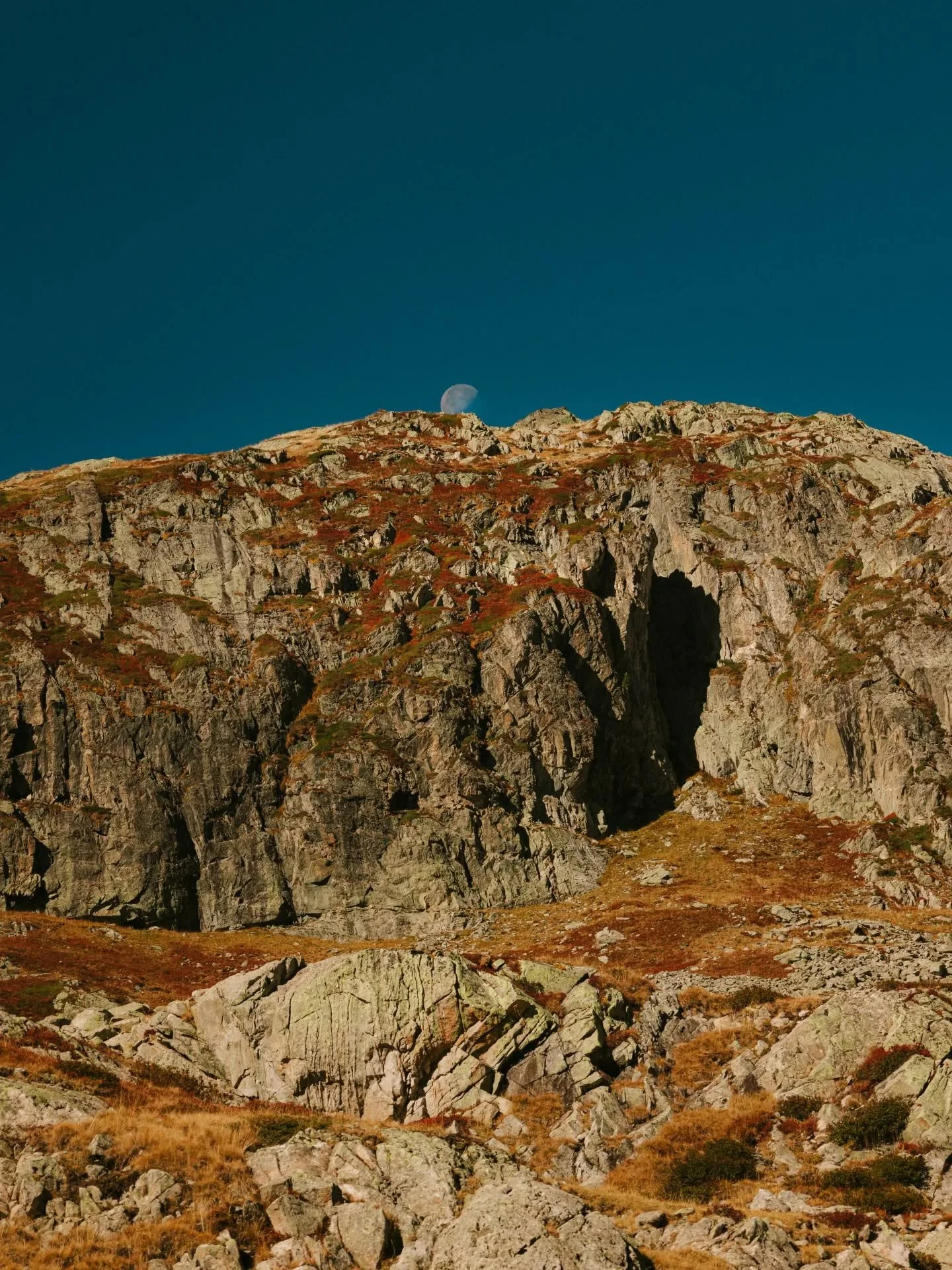 Montagne rocheuse avec un ciel bleu et la lune visible en arrière-plan.