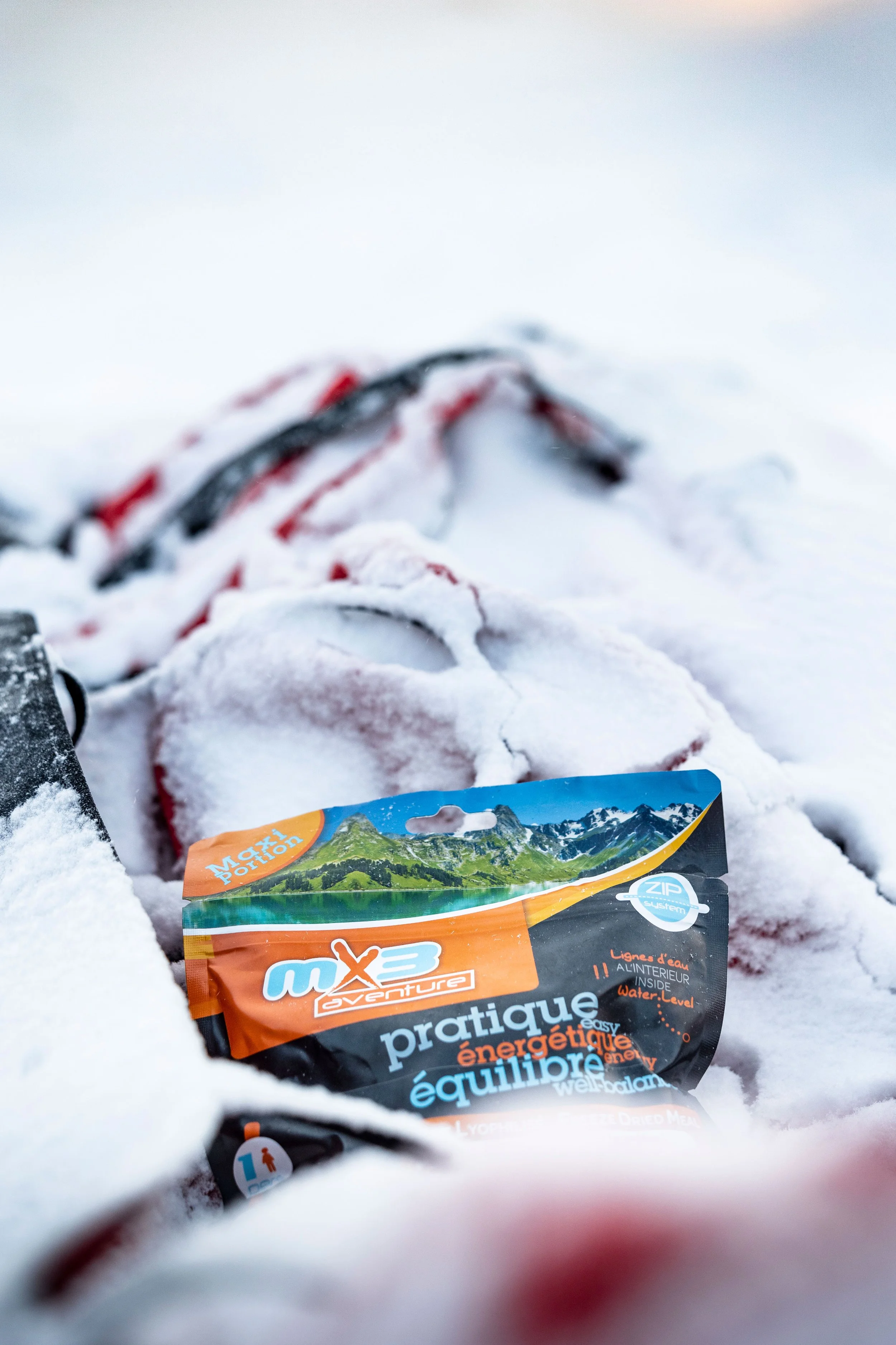 Un sachet énergétique posé sur la neige, avec des skis en arrière-plan, dans un environnement enneigé.