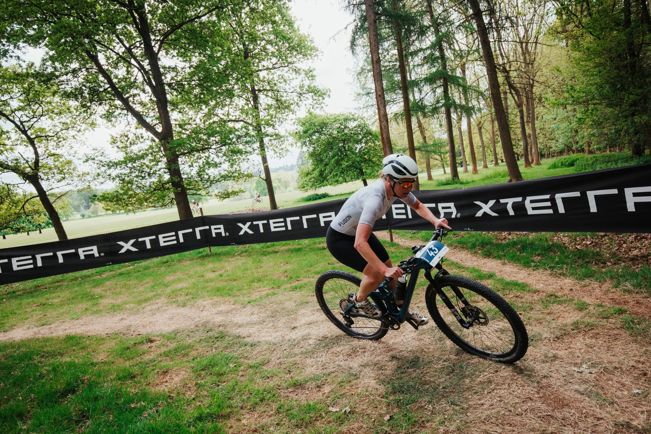 Coureuse sur un vélo de montagne lors d'une course en plein air dans une forêt verdoyante, portant un casque et une tenue sportive