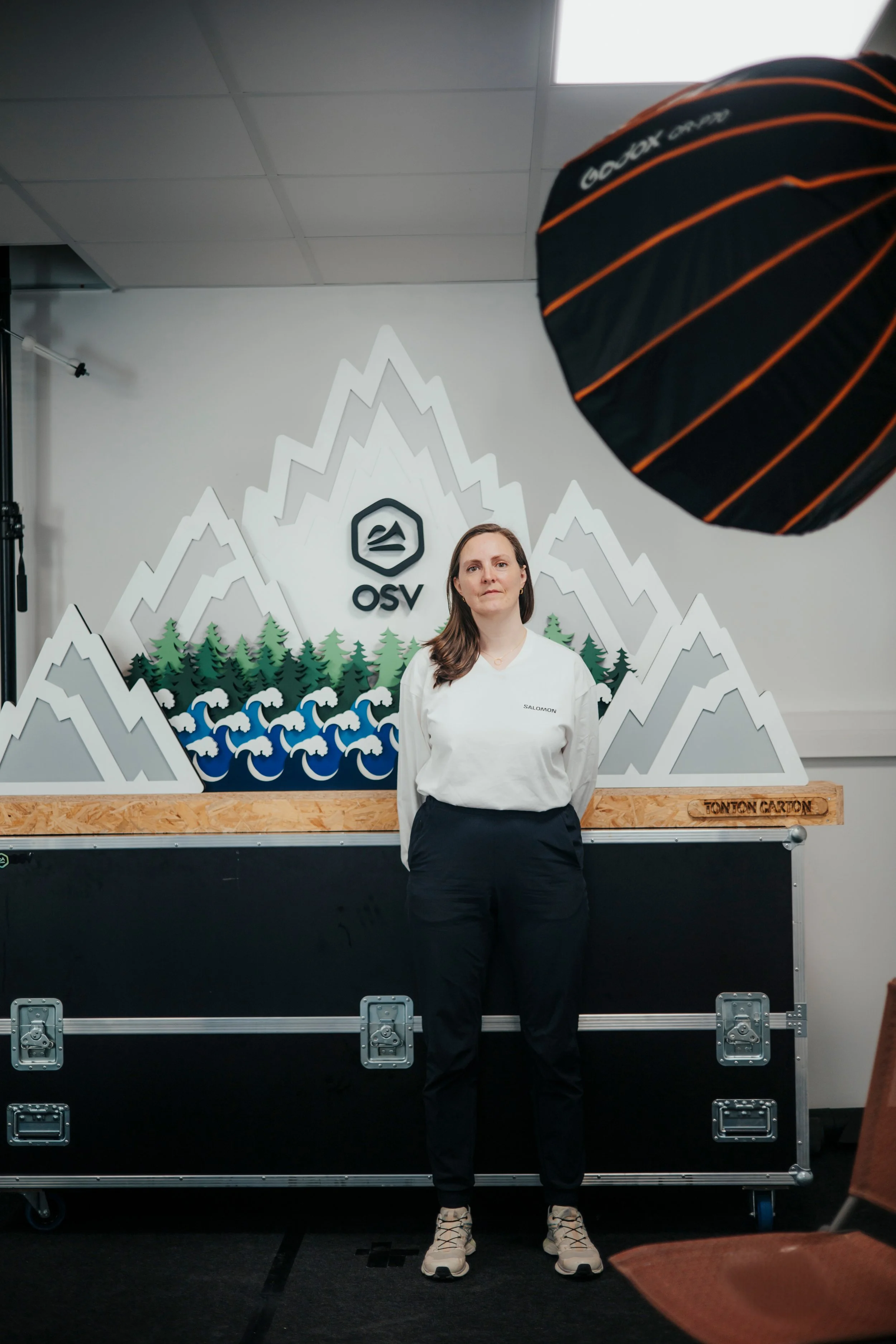 Une femme posant devant un décor avec montagnes, arbres, vagues, et le logo OSV.