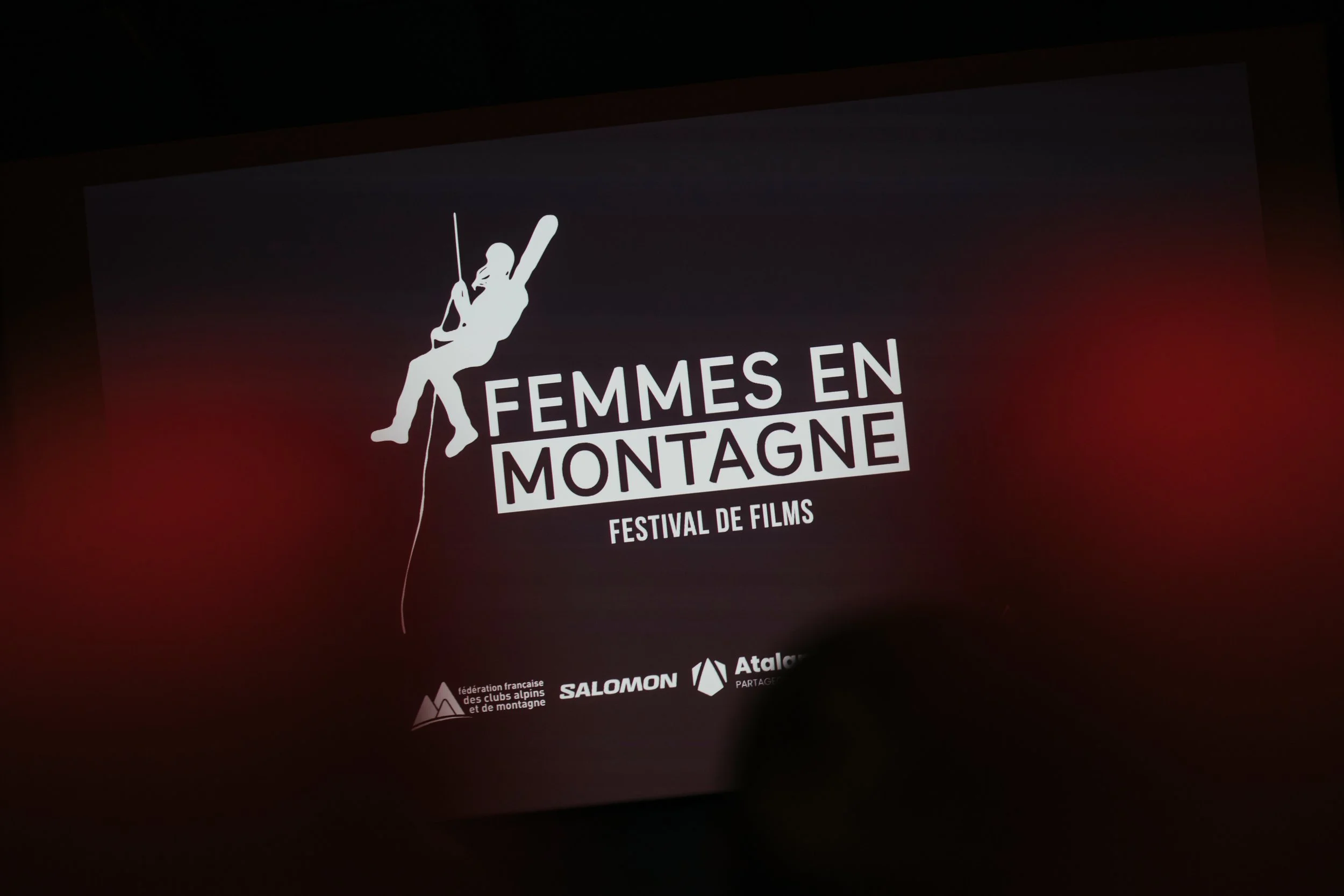 Affiche du festival de films 'Femmes en Montagne' avec un logo de femme grimpeuse en silhouette