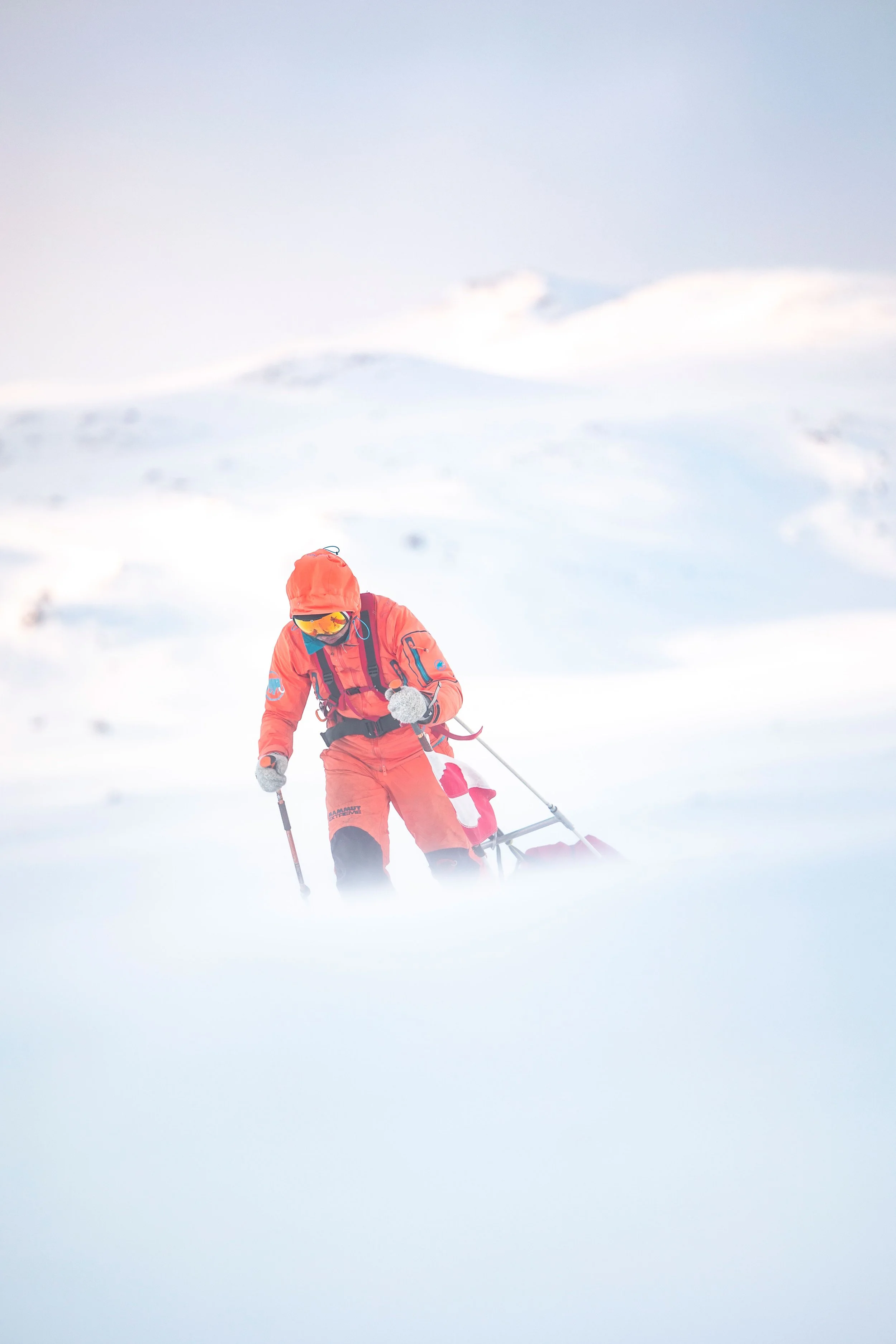 Une personne en tenue de ski orange poussant une luge dans un paysage enneigé et brumeux.