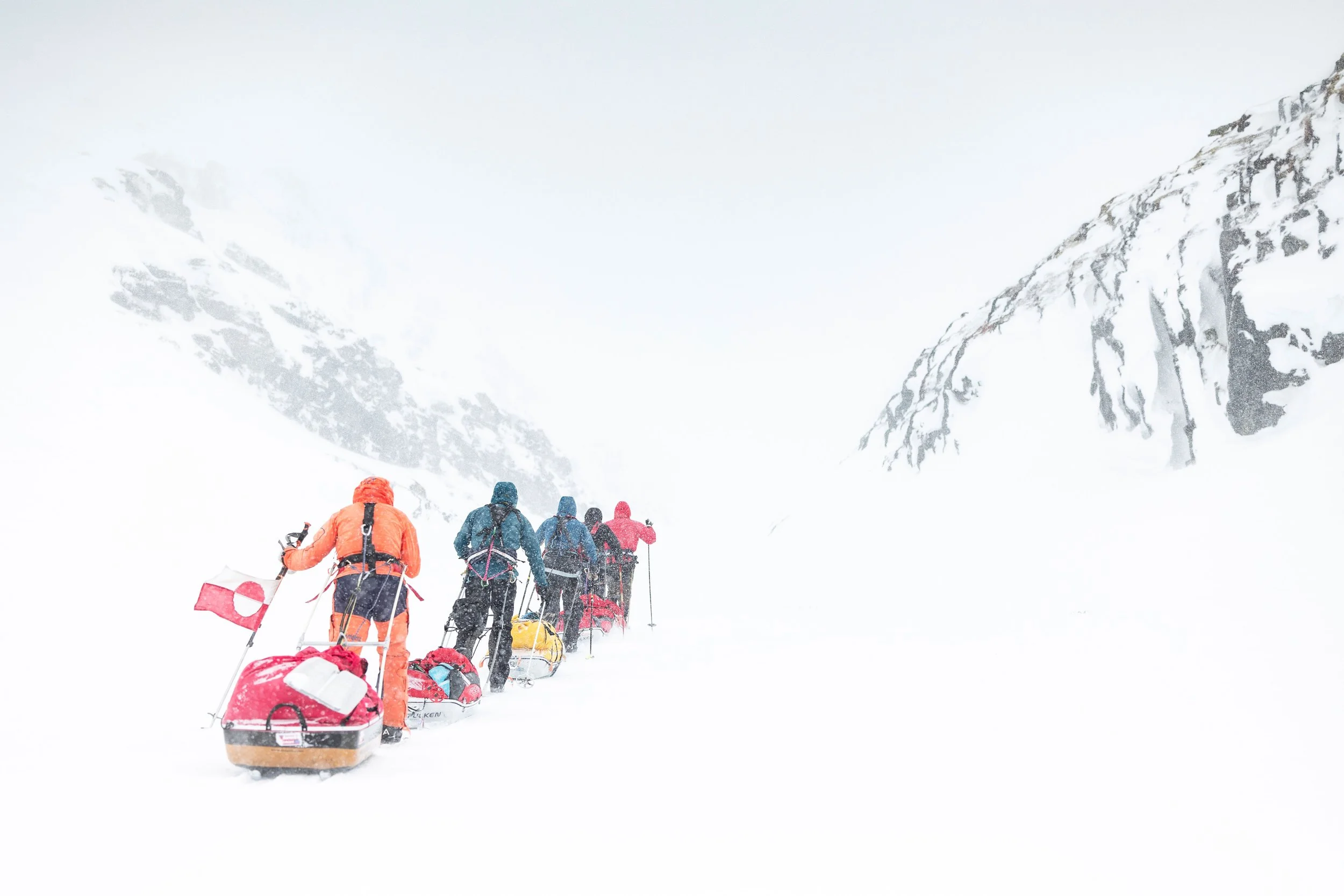 Groupe de randonneurs en traîneau à neige dans un paysage enneigé avec des montagnes en arrière-plan.