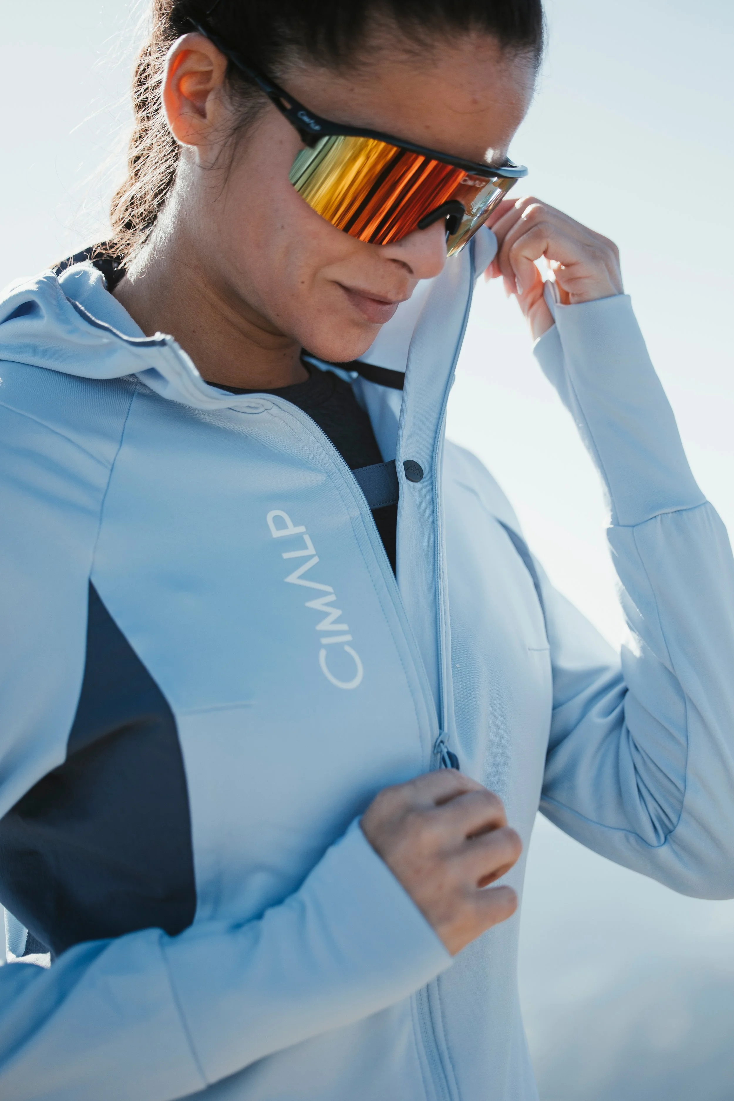 Femme portant un équipement de sport, notamment une veste bleue, des lunettes de soleil de course, prêt à faire de l'exercice en extérieur.