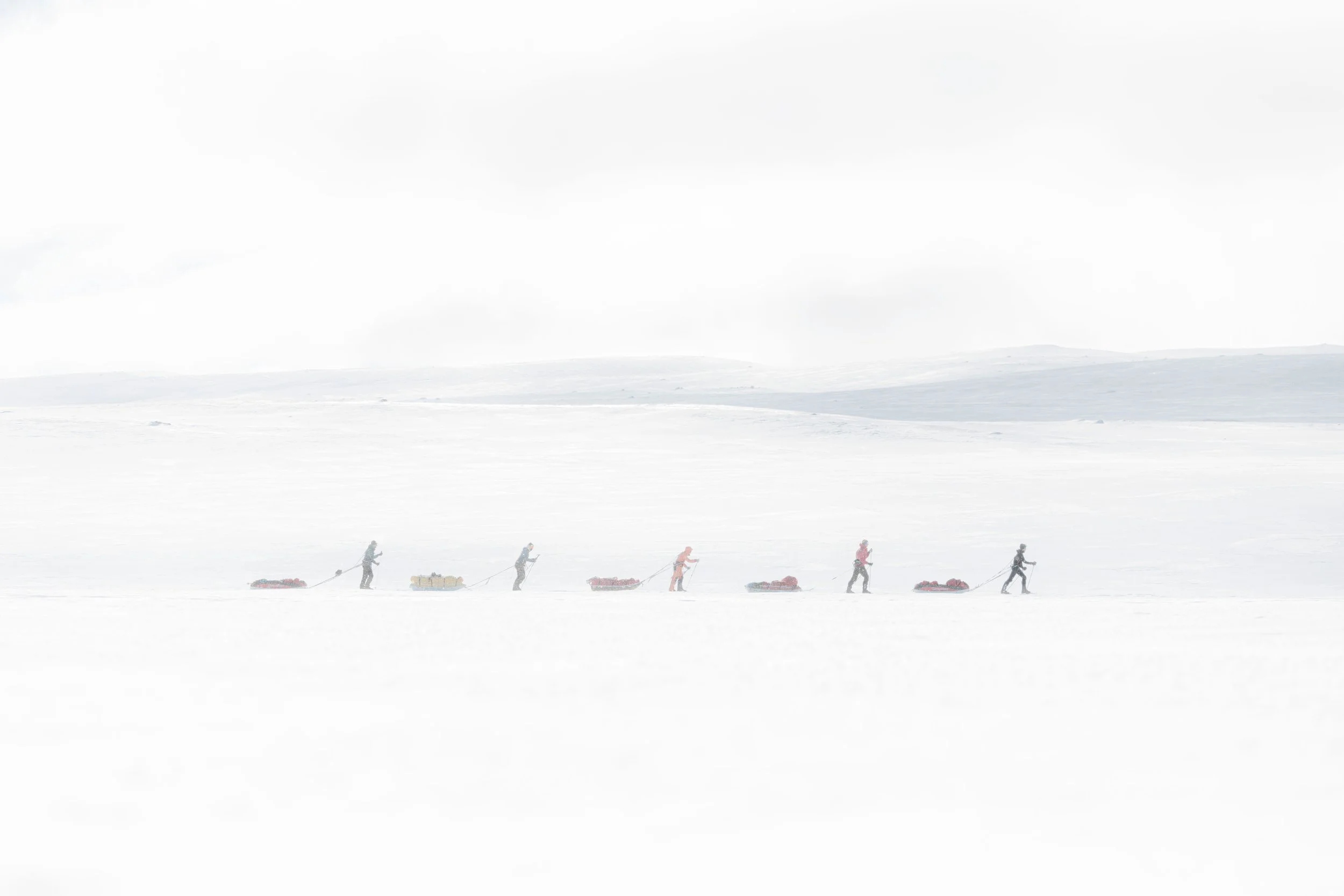 Groupe de personnes avançant dans un paysage enneigé, tirant des traîneaux avec des équipements.