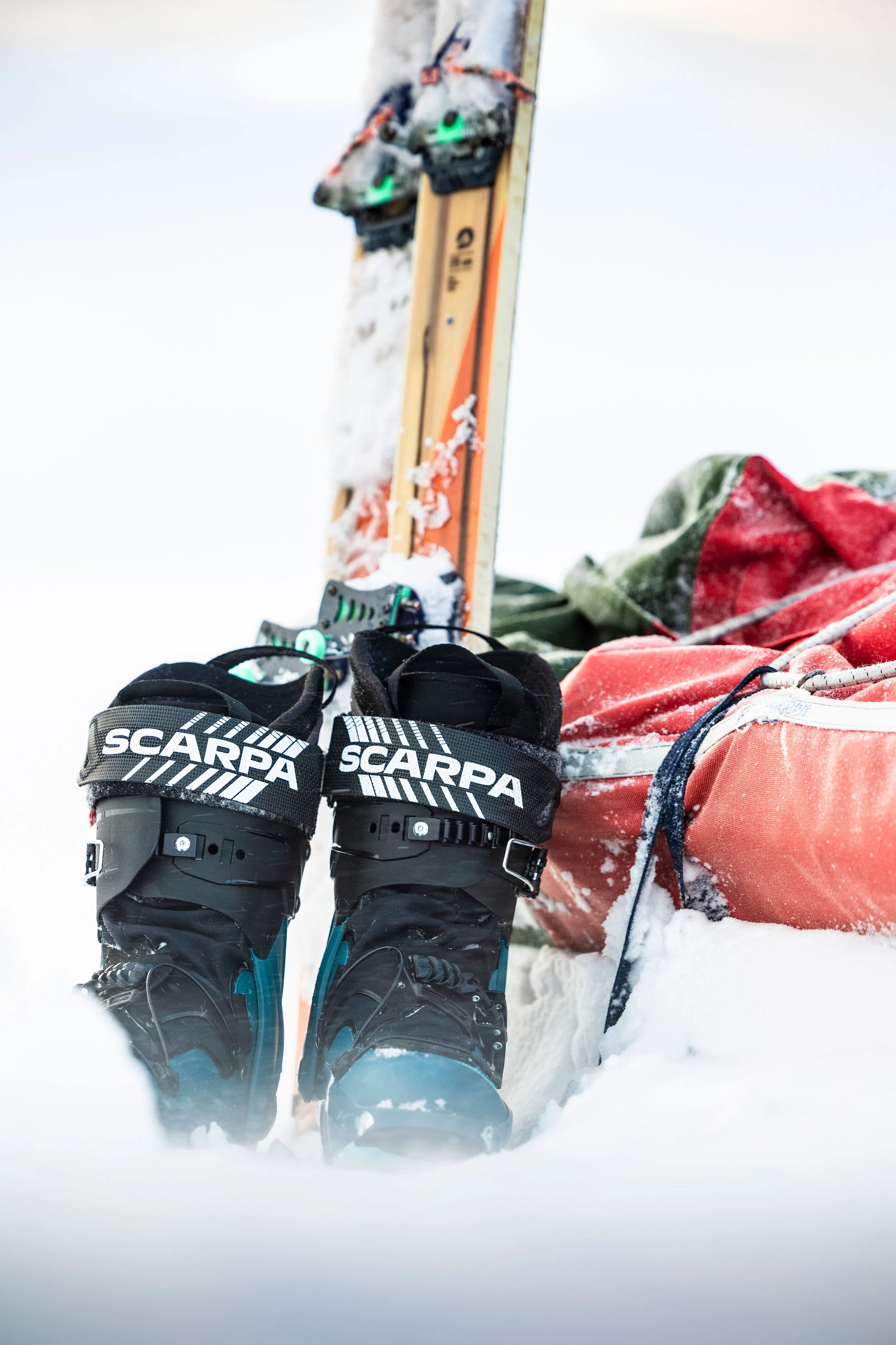 Bottes de ski Scarpa, sac à dos et skis posés dans la neige, vêtements de ski visibles, équipement de ski dans un environnement enneigé.