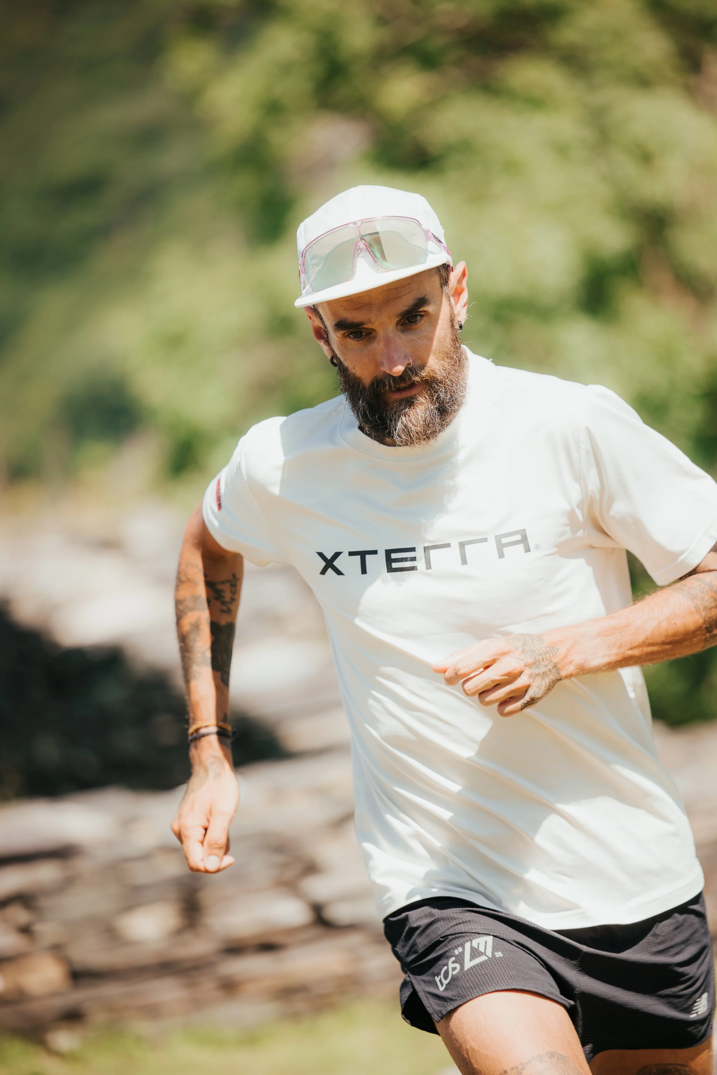 Un homme, Yoann Stuck, qui court dans un environnement naturel avec des arbres en arrière-plan, portant une casquette blanche, des lunettes de soleil sur la tête, un t-shirt blanc avec le mot en anglais 'XTERRA', et des shorts noirs.