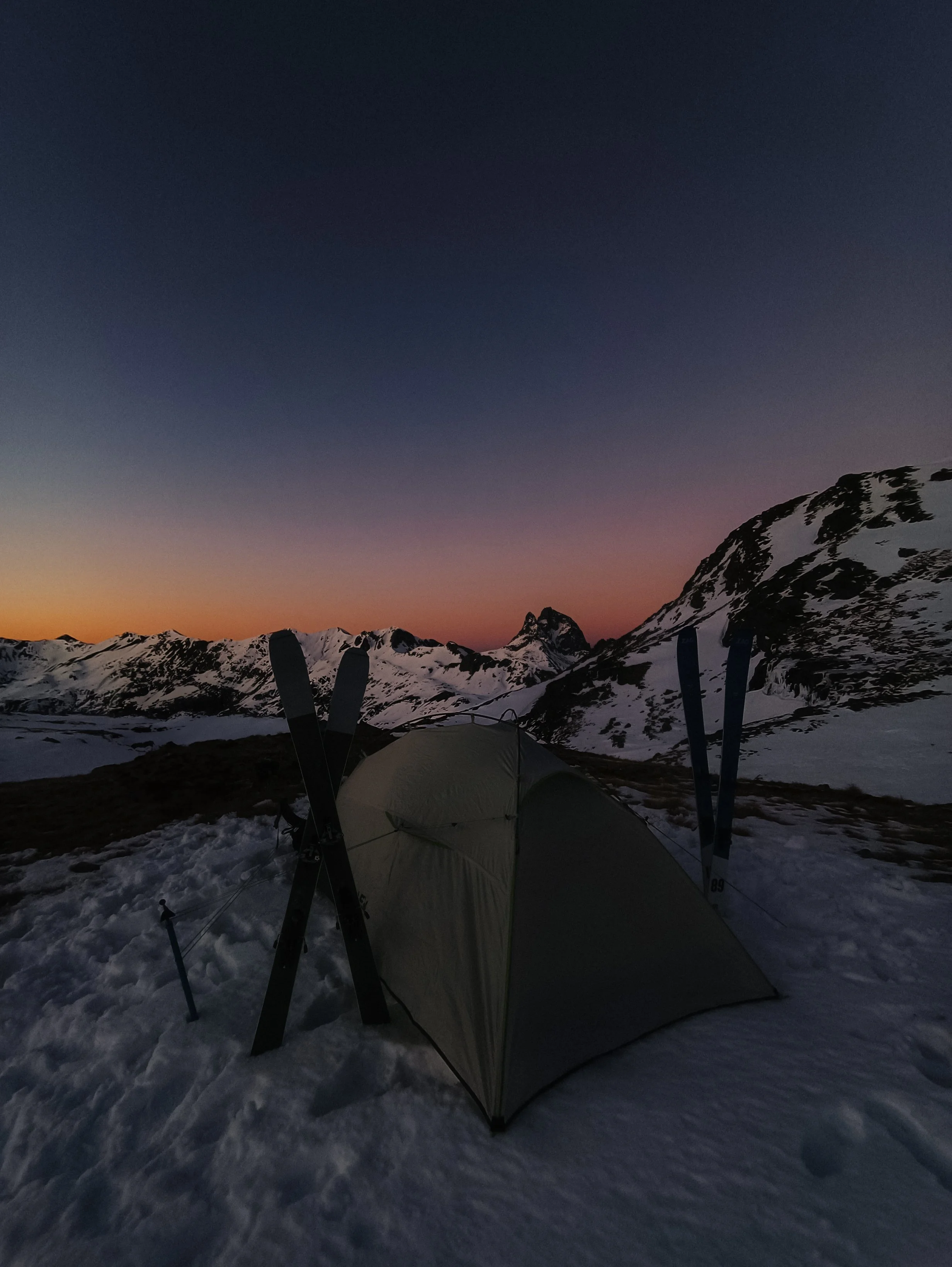 Une tente dans un paysage enneigé avec des montagnes au coucher du soleil.