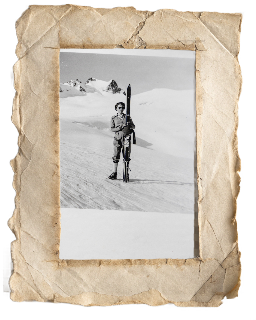 Une personne portant des vêtements d'hiver, tenant des skis, dans un paysage de neige avec des montagnes en arrière-plan.