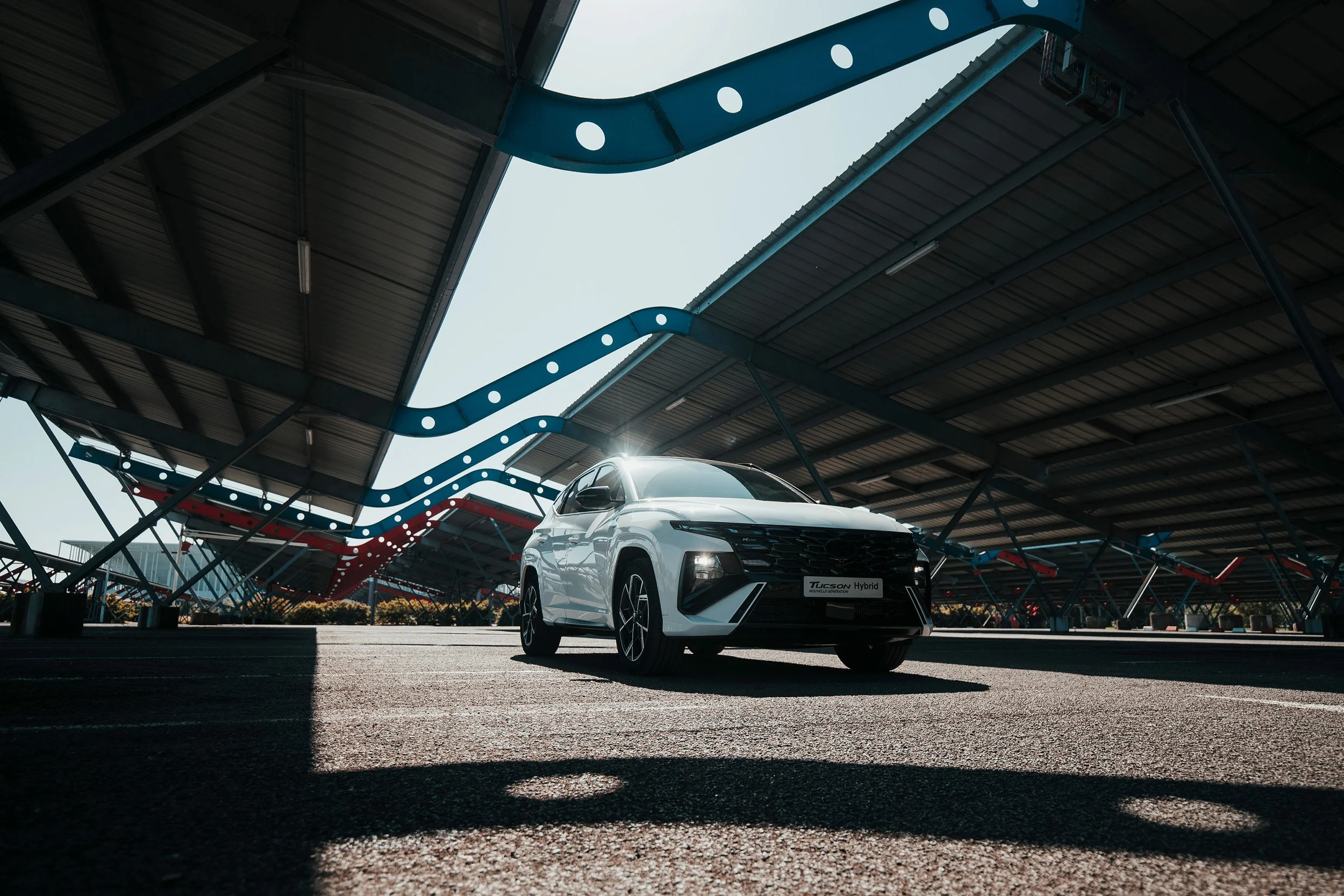 Voiture blanche Hyundai Tucson Hybrid stationnée dans un parking avec un toit métallique en structural exposée