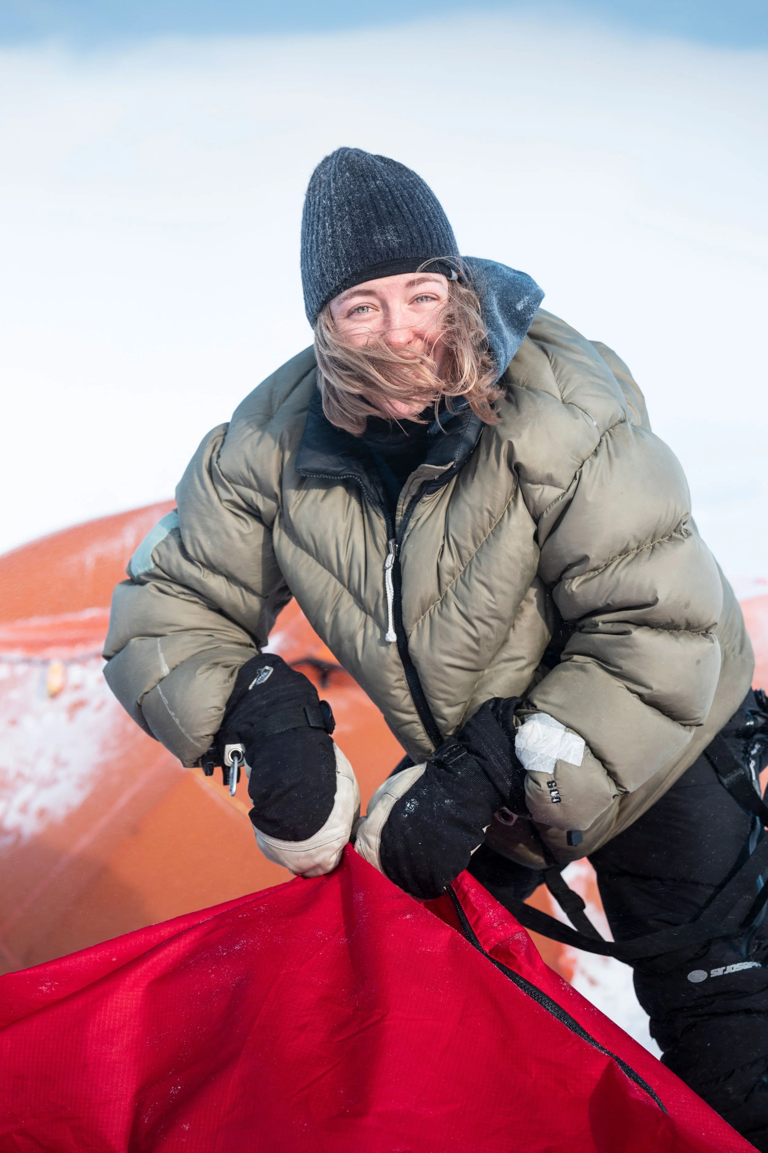 Une femme en vêtements d'hiver déployant une tente par temps froid et neigeux.