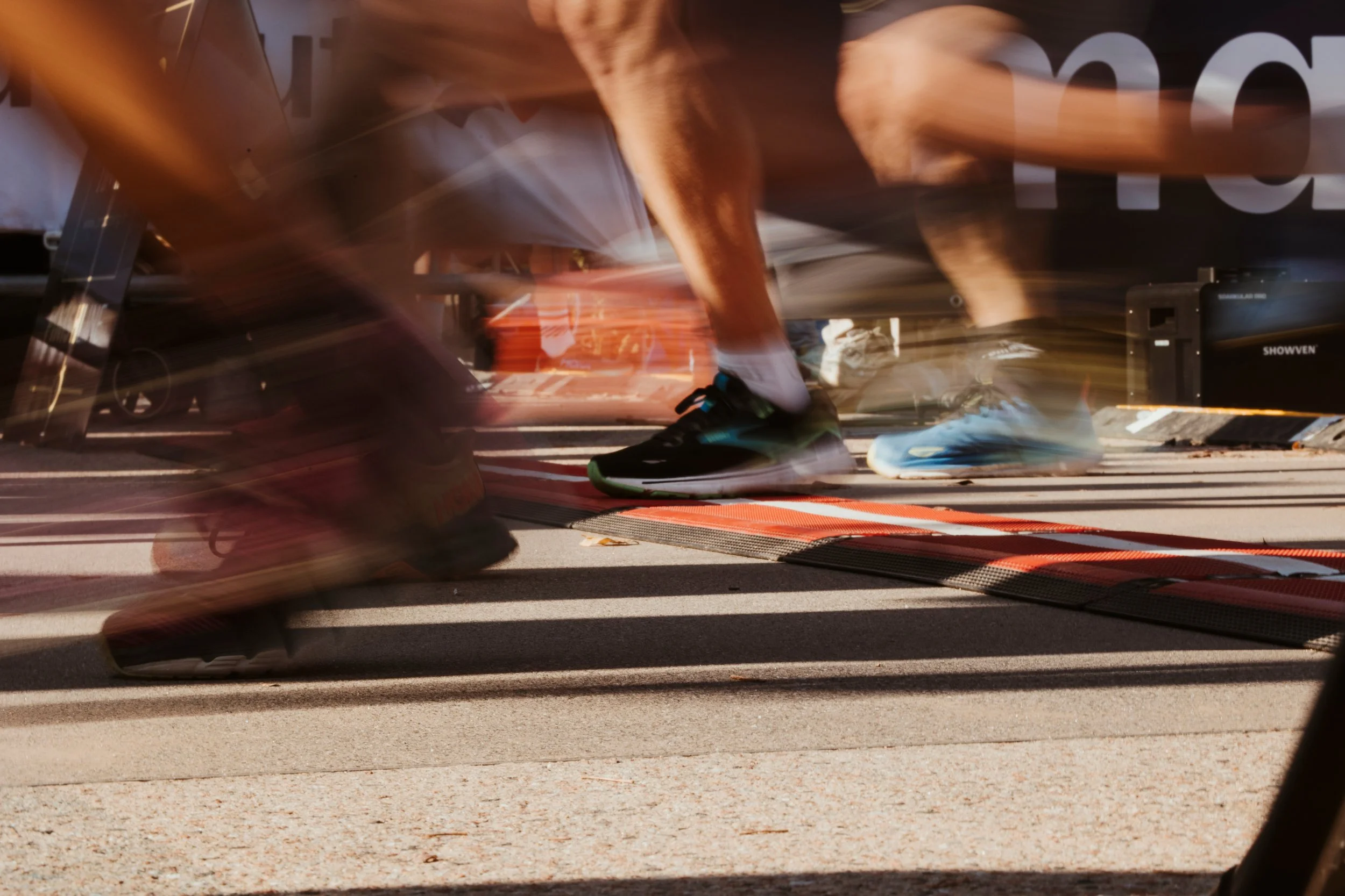 Coureurs à pied en mouvement, portant des chaussures de course, lors d'une course ou d'un entraînement, avec des lignes d'arrivée ou une zone de départ visible au sol.