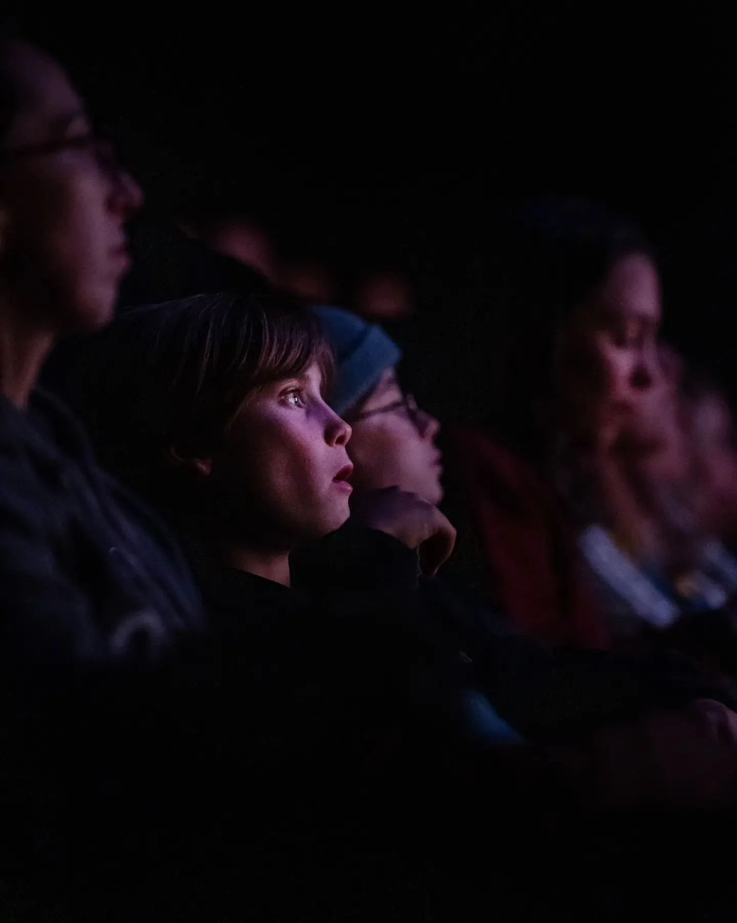 Groupe de personnes regardant un spectacle ou un film dans une salle sombre, avec une attention concentrée.