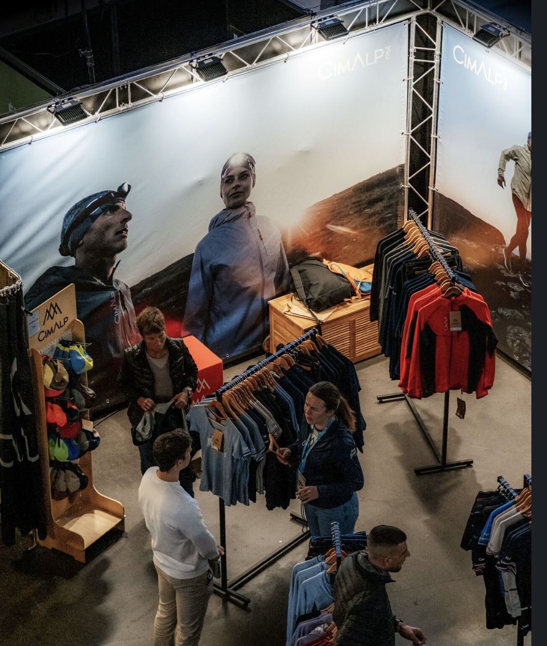 Vendeurs et clients dans un magasin de sport outdoor avec une grande bannière pour la marque CIMALP, affichant des personnes en pleine nature.