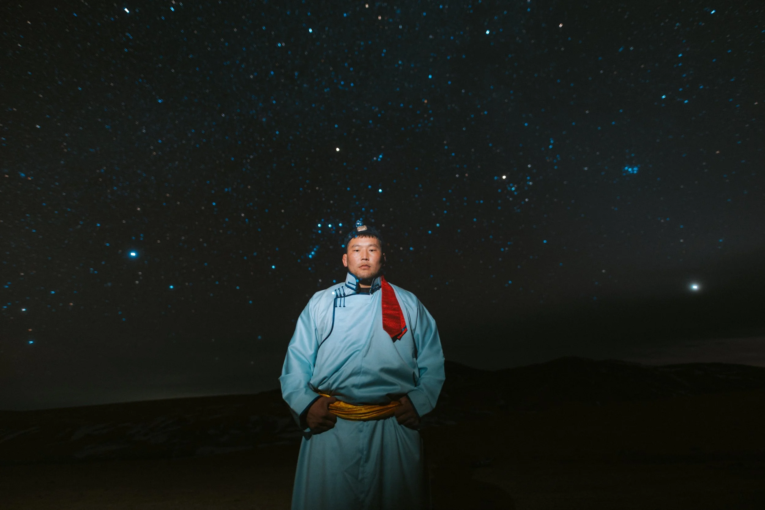 Homme en tenue traditionnelle devant un ciel étoilé nocturne.