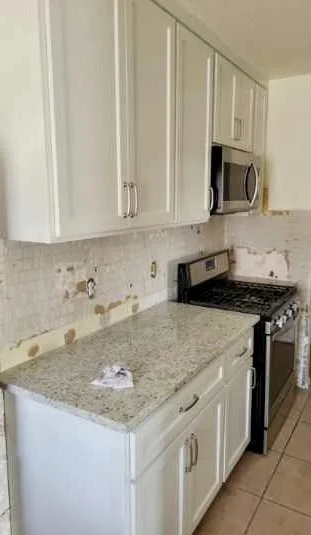 Kitchen with white cabinets, a granite countertop, and a black stove with a microwave above it. The backsplash appears to be unfinished.
