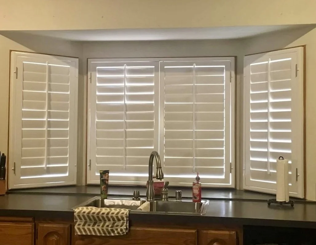 Kitchen window with white plantation shutters and black countertop, with a soap dispenser, paper towel roll, and kitchen sink.