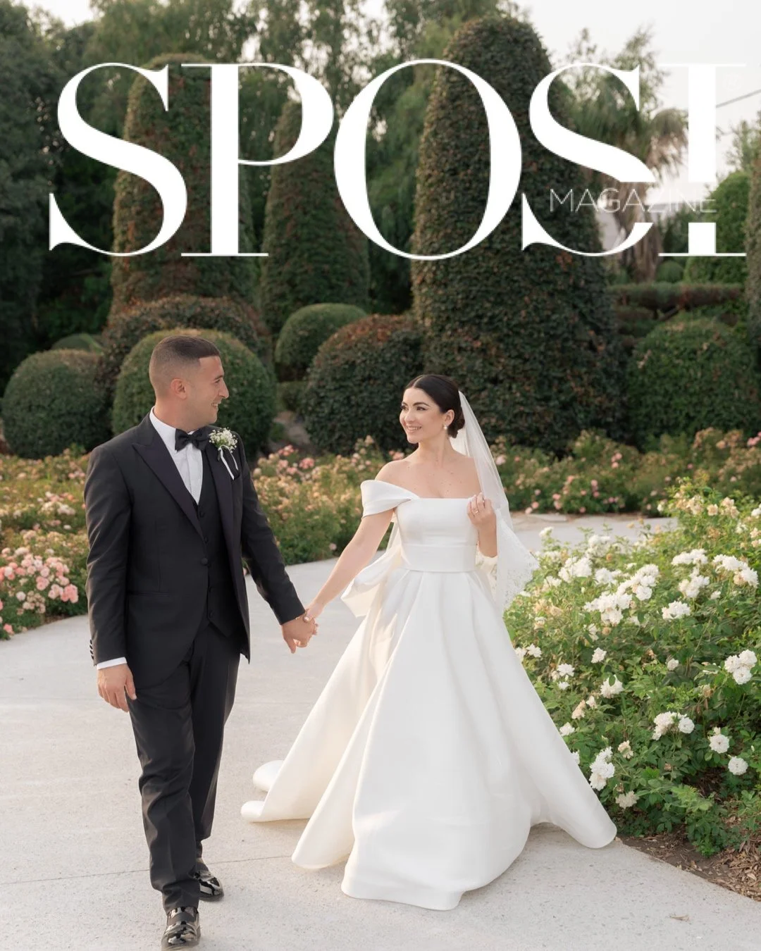Una coppia in abito da sposa e da uomo che si tiene per mano in un giardino con fiori e arbusti ben curati.