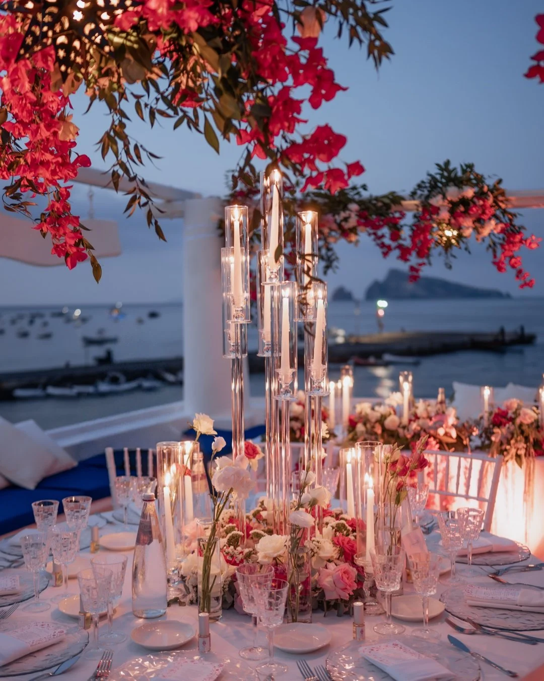 Un tavolo decorato con fiori e candele, vicino a un mare in un ambiente serale o notturno.