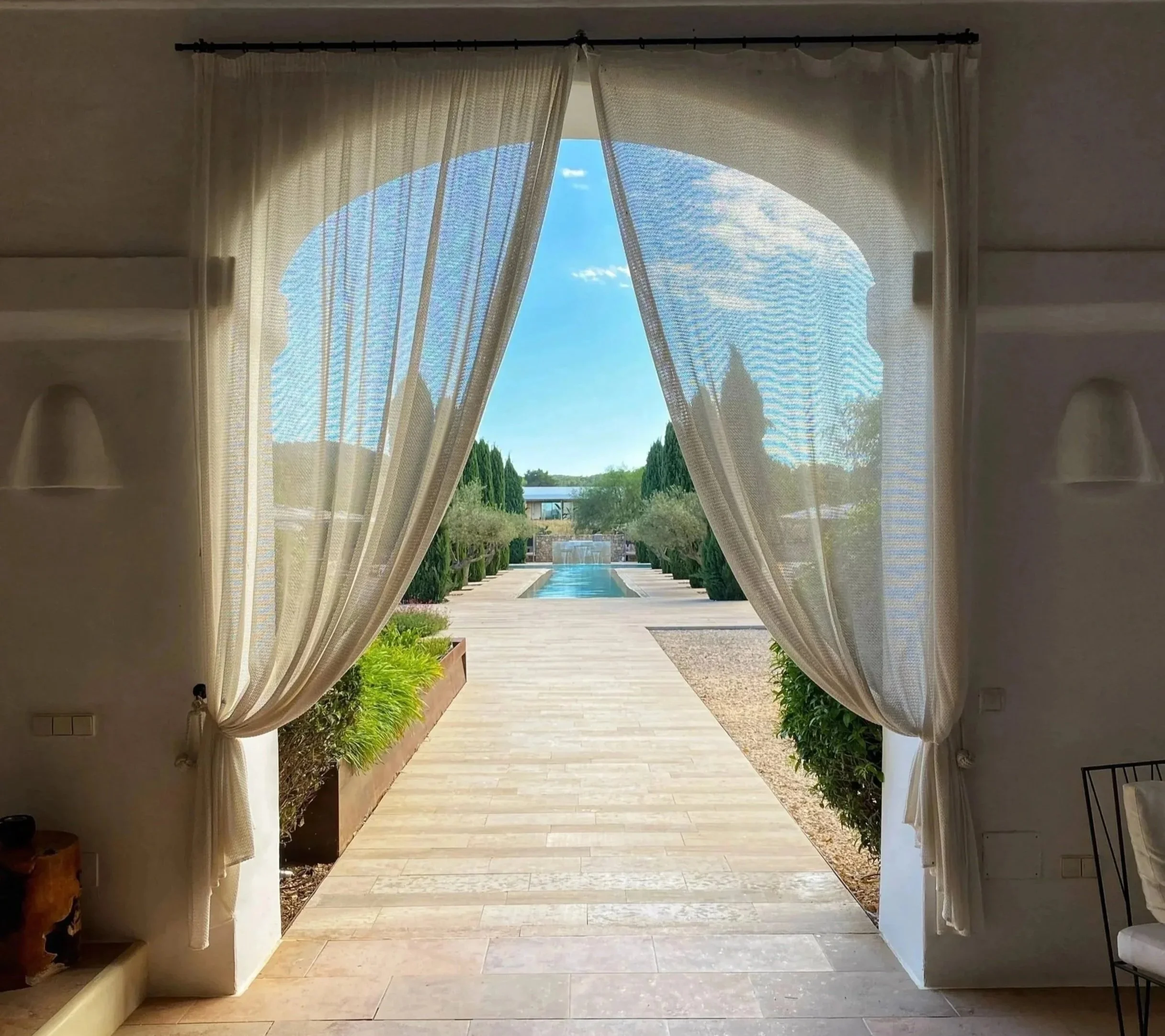 View through an open doorway showing a pathway, greenery, and a fountain outdoors on a sunny day.