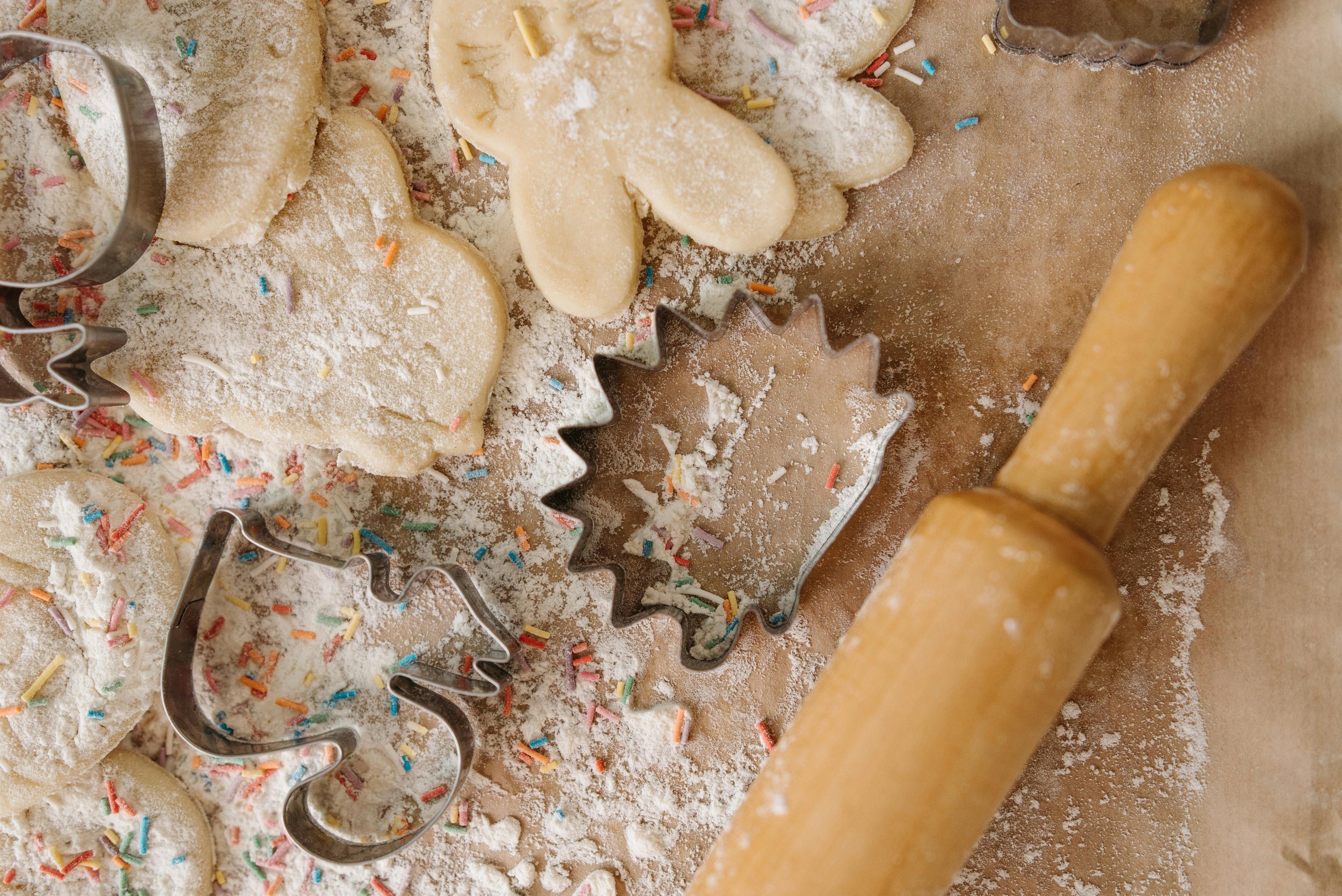 Close-up of a floured countertop with sugar cookie cutouts and sprinkles - Merry Berry Confection Co. | Micro-bakery specializing in holiday bakes + dessert bars for weddings + events | Cary, NC