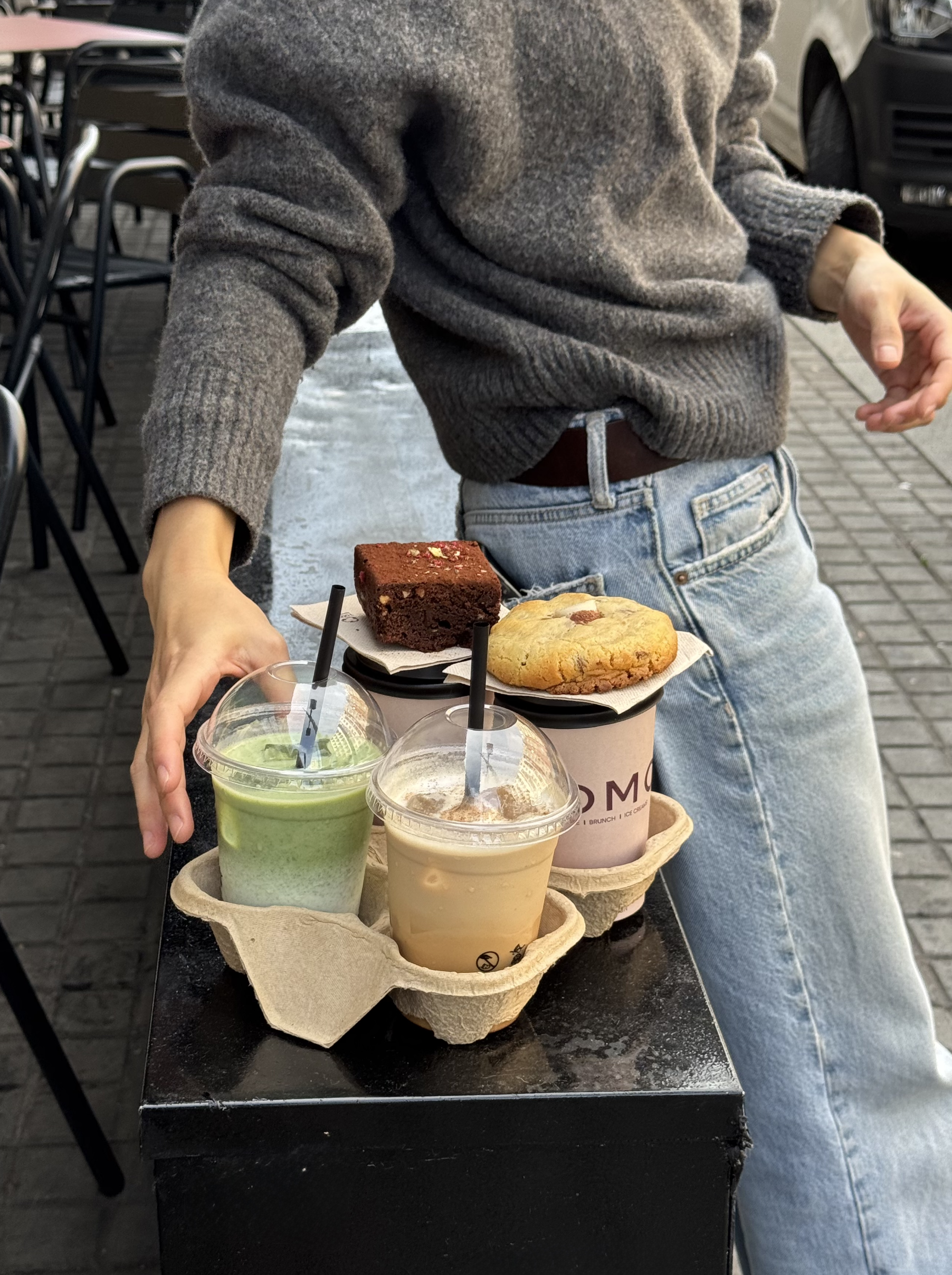 Persona sirviendo una bandeja con bebidas en vasos con tapas plásticas y tres postres.