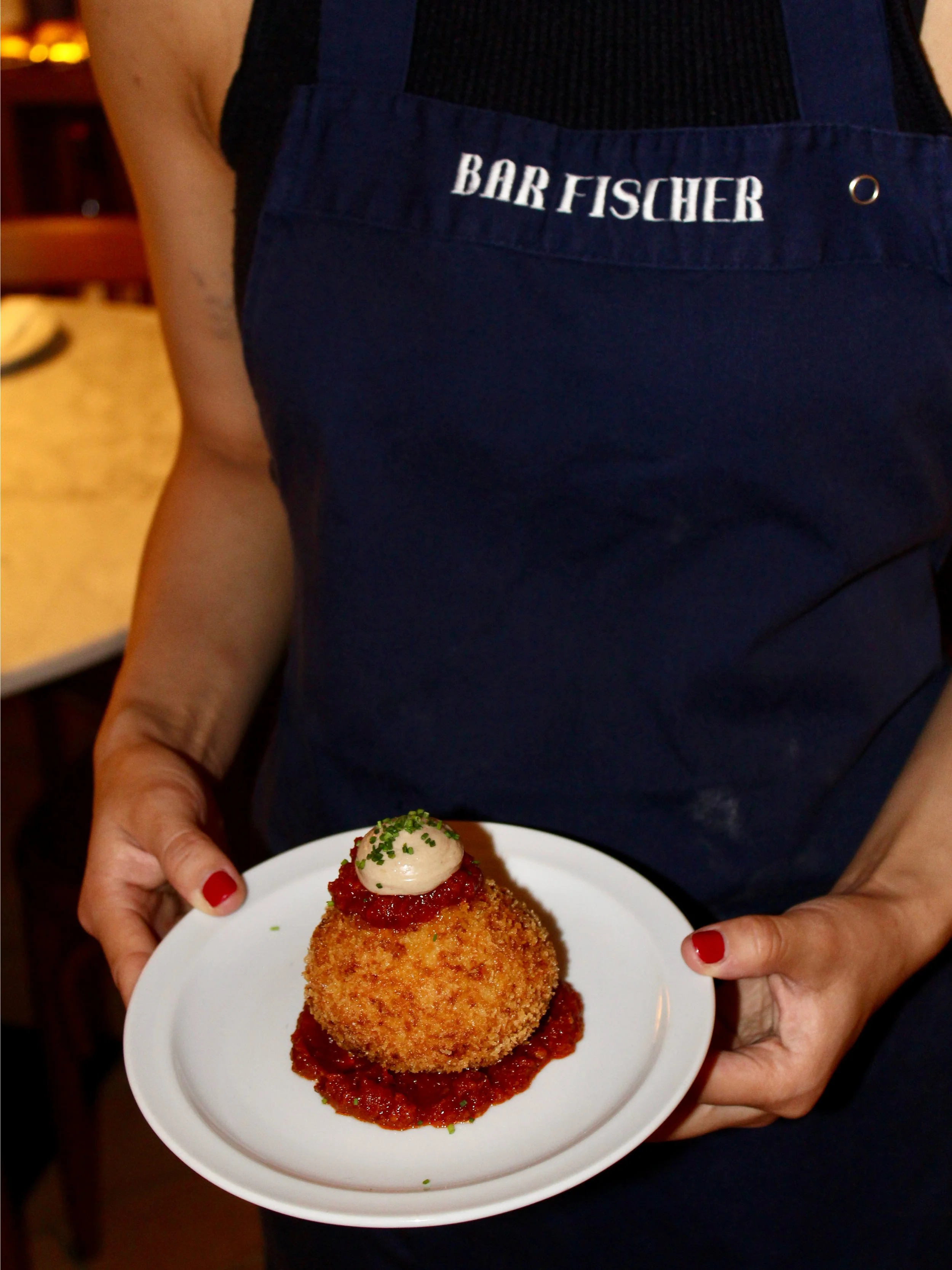 Una persona con un delantal de 'BAR FISCHER' sostiene un plato con comida