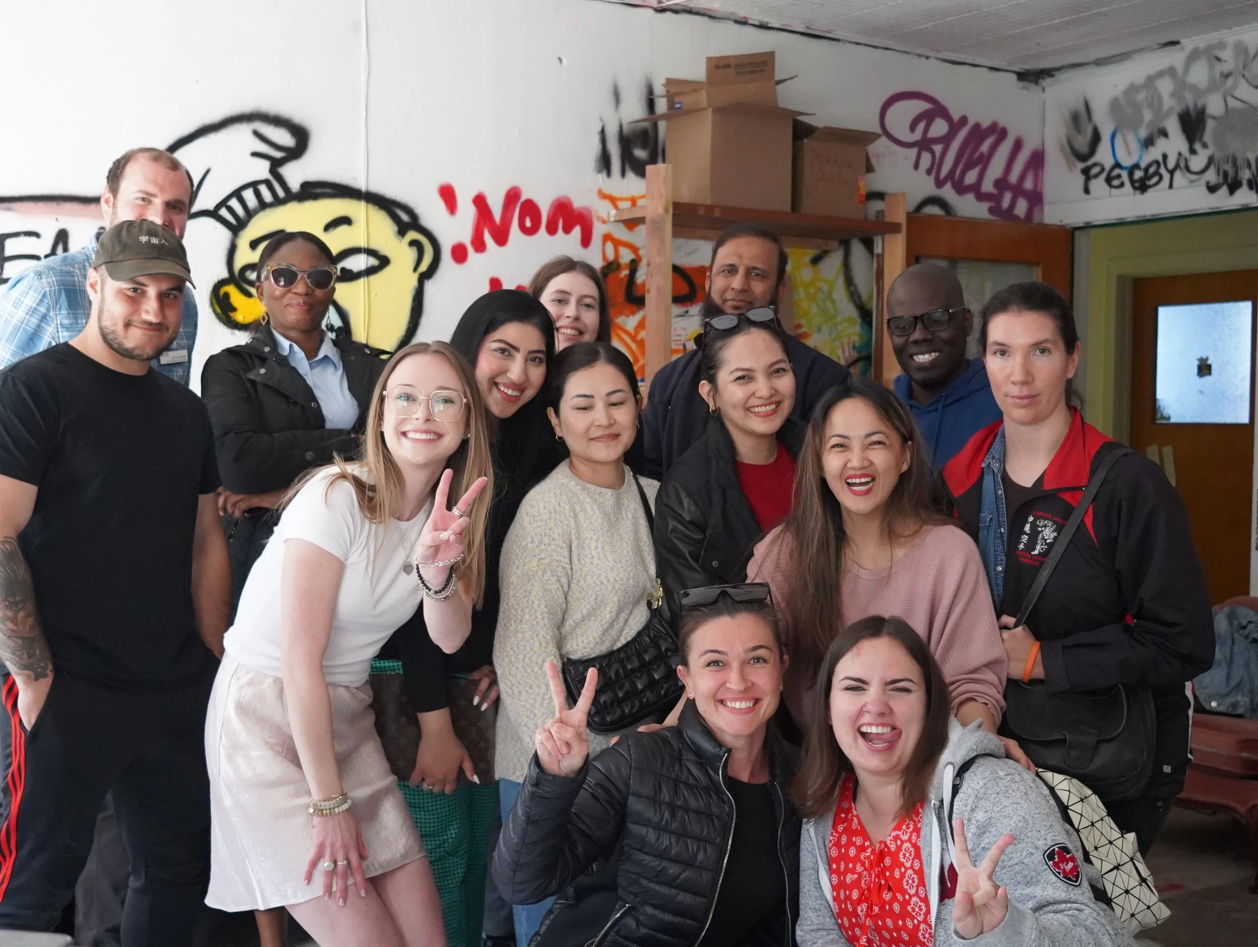 A group of diverse people smiling and posing together inside a room with graffiti on the walls.