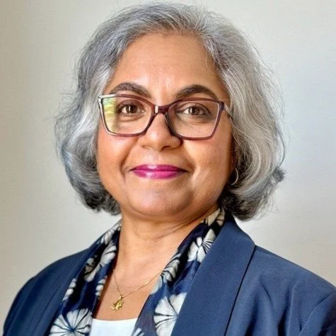 A portrait of a middle-aged woman with gray hair, glasses, and pink lipstick, wearing a blue blazer and a patterned scarf.