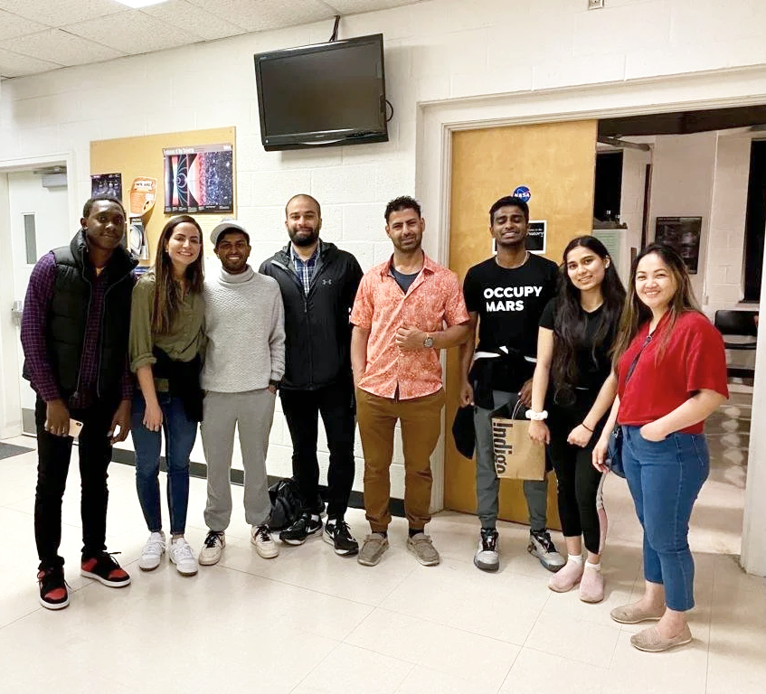Group of eight diverse young adults standing in school hallway.