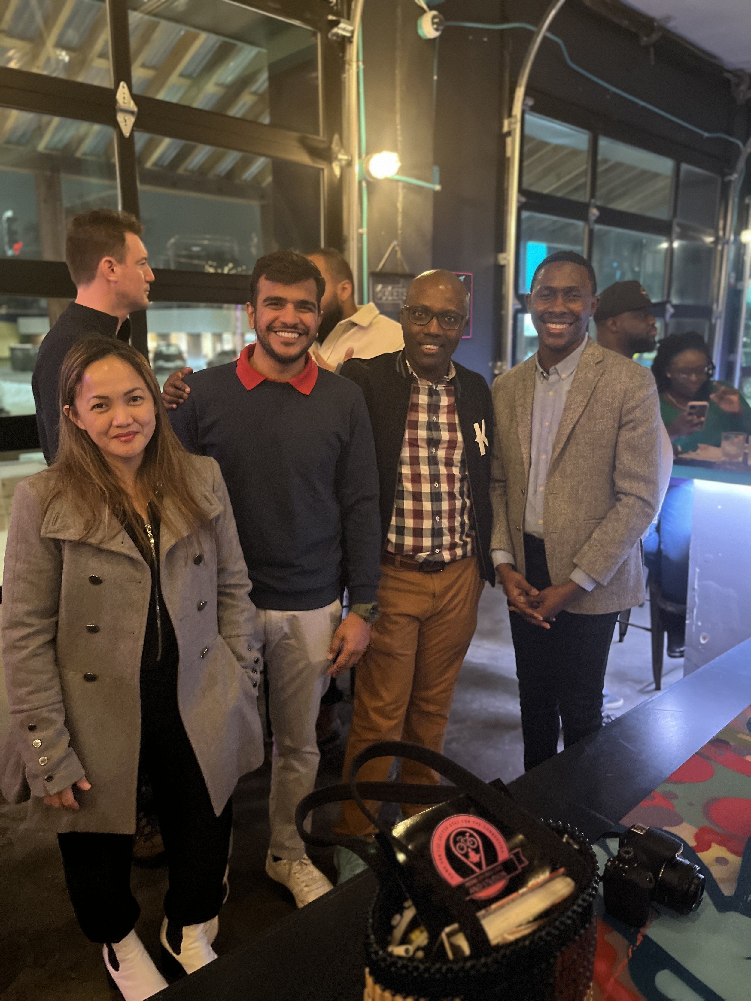 Group of five diverse people smiling and standing together indoors at a social event or party.
