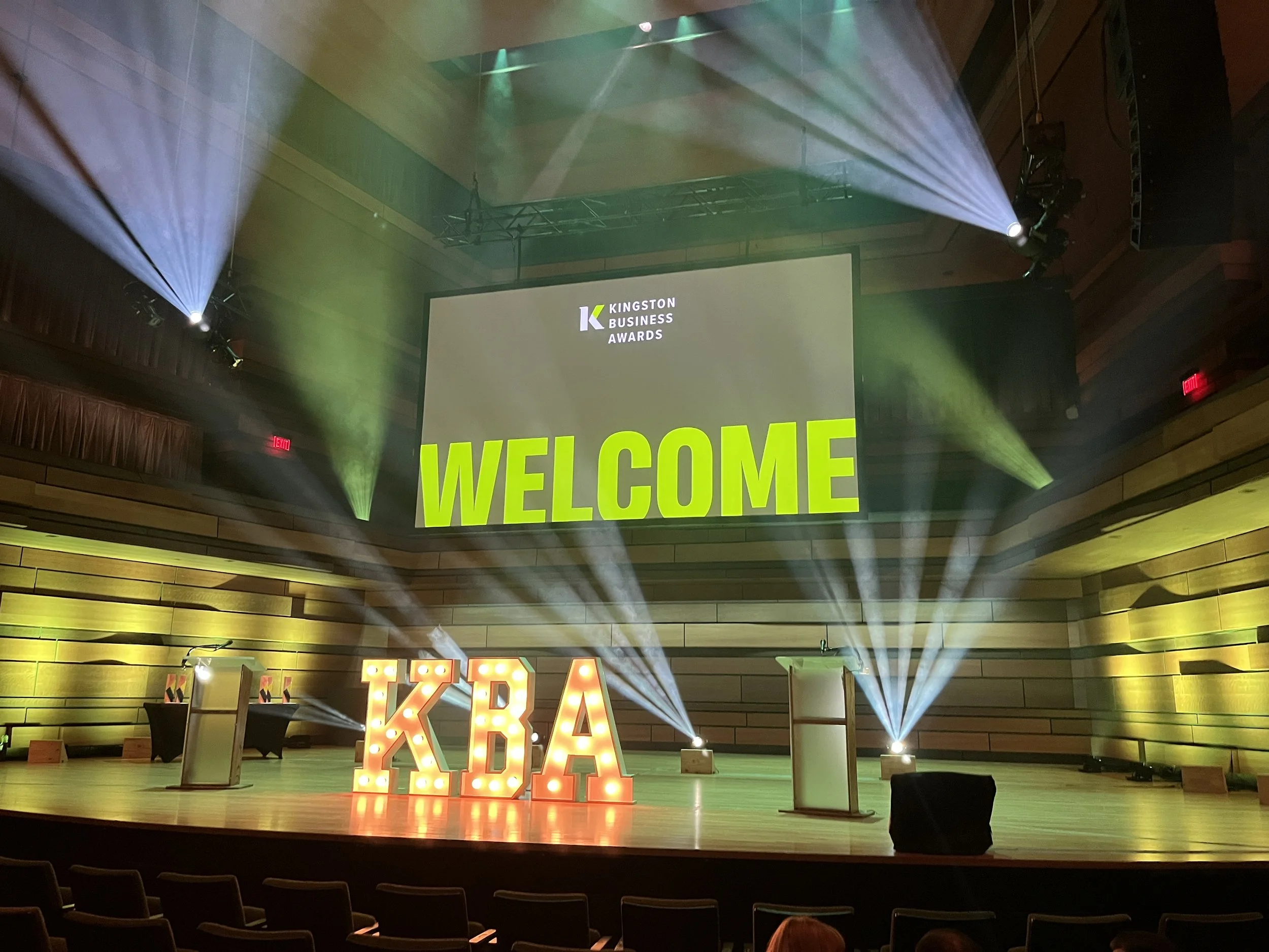 Stage with a large screen displaying "WELCOME" at the Kingston Business Awards, illuminated KBA letters, and stage lights