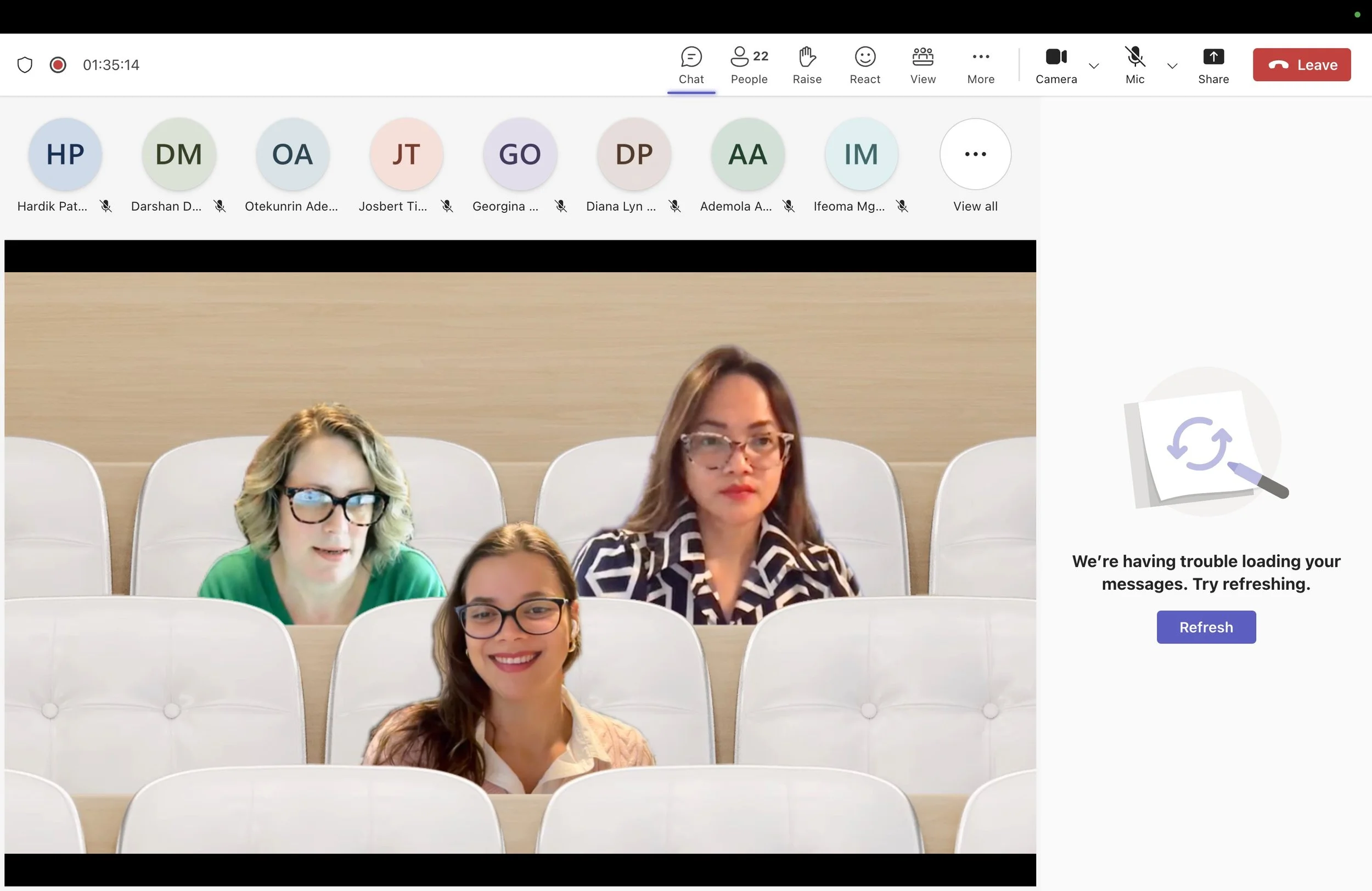 A screenshot of a virtual meeting with three women, two in the front row and one behind, all wearing glasses, seated in white chairs in front of a beige background, with a message indicating trouble loading messages on the right side of the screen.