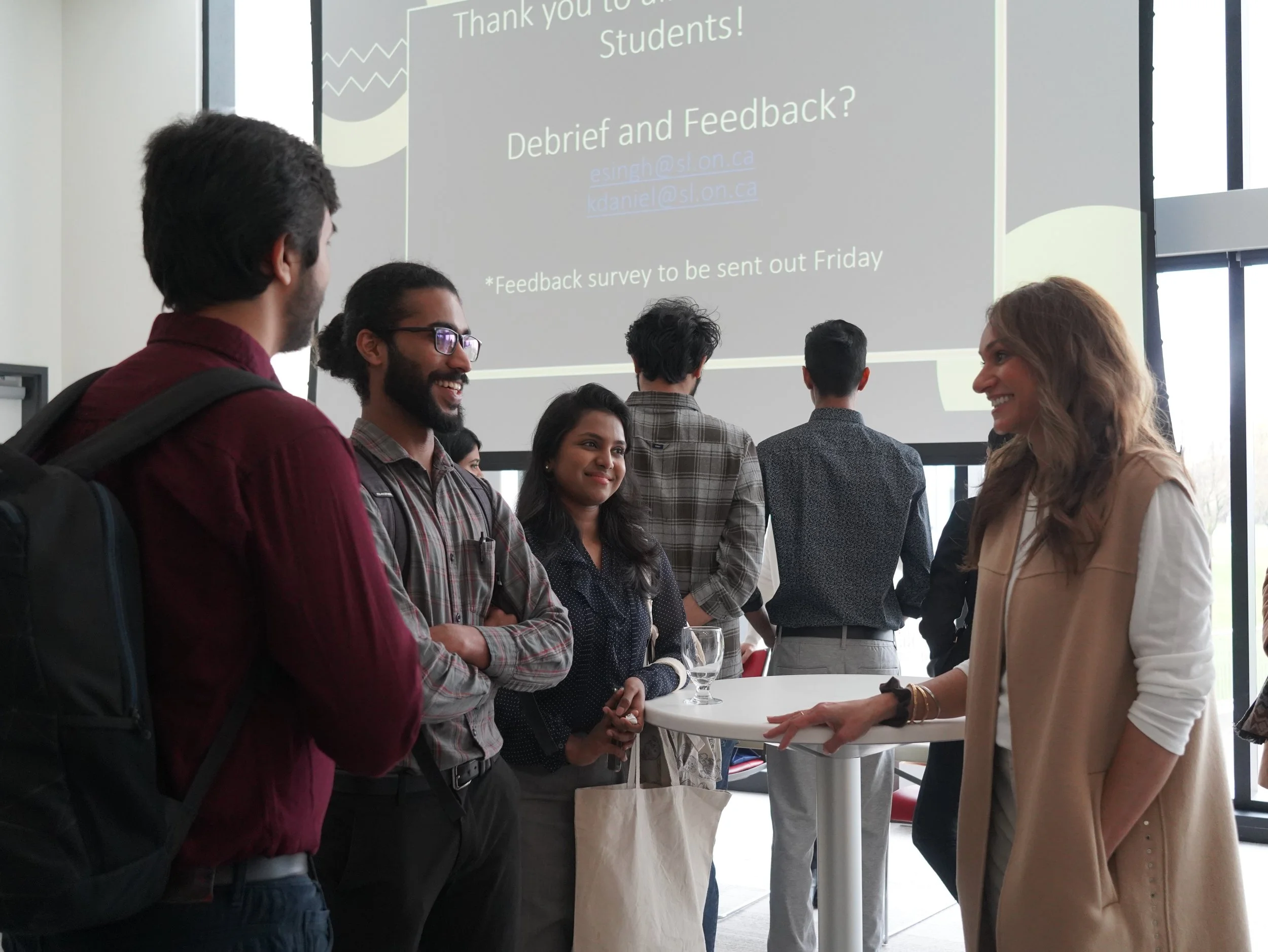 Group of diverse students talking and smiling in a modern indoor setting at a college or university event.