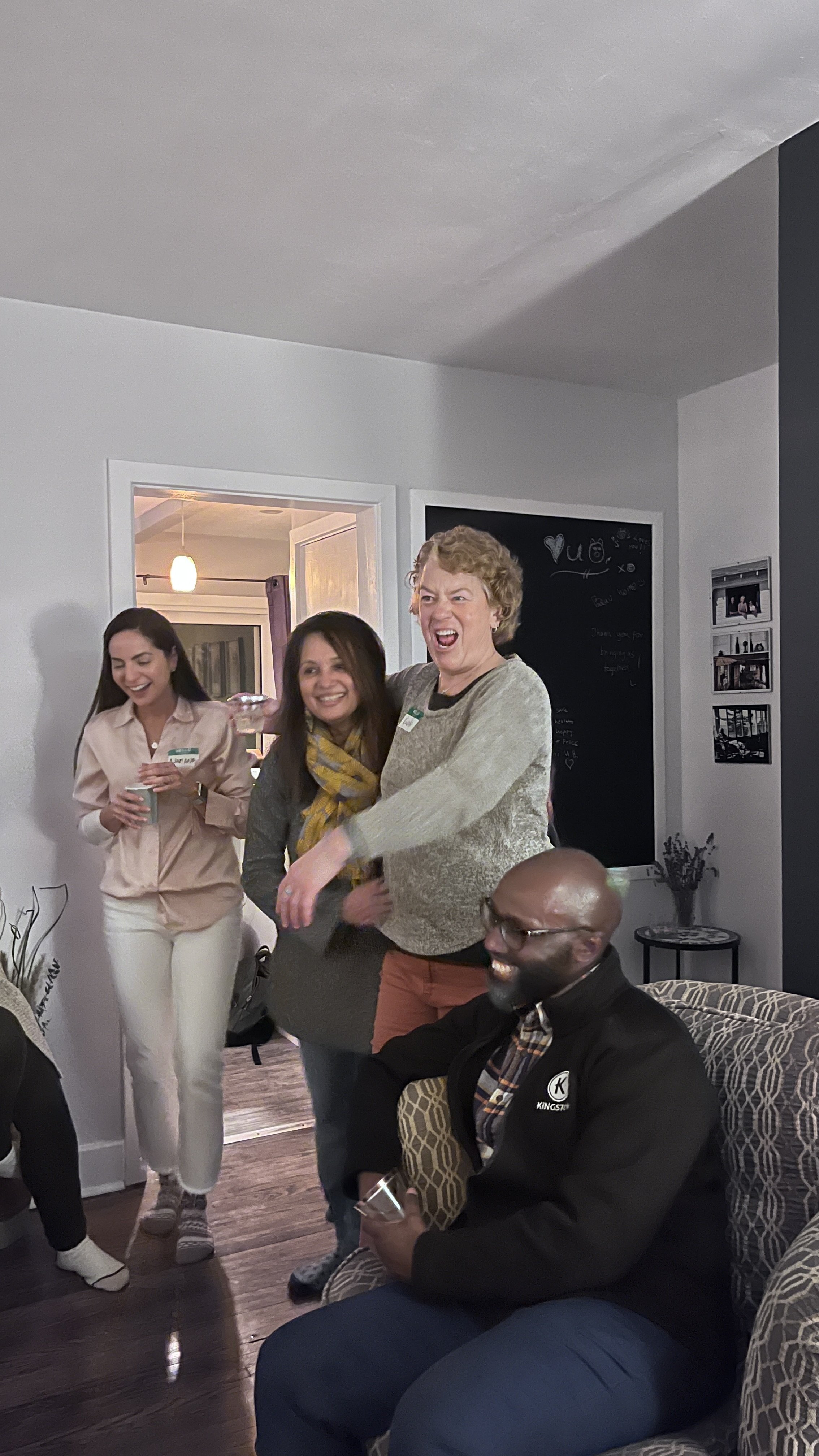 Group of friends enjoying a social gathering in a living room, smiling and laughing.