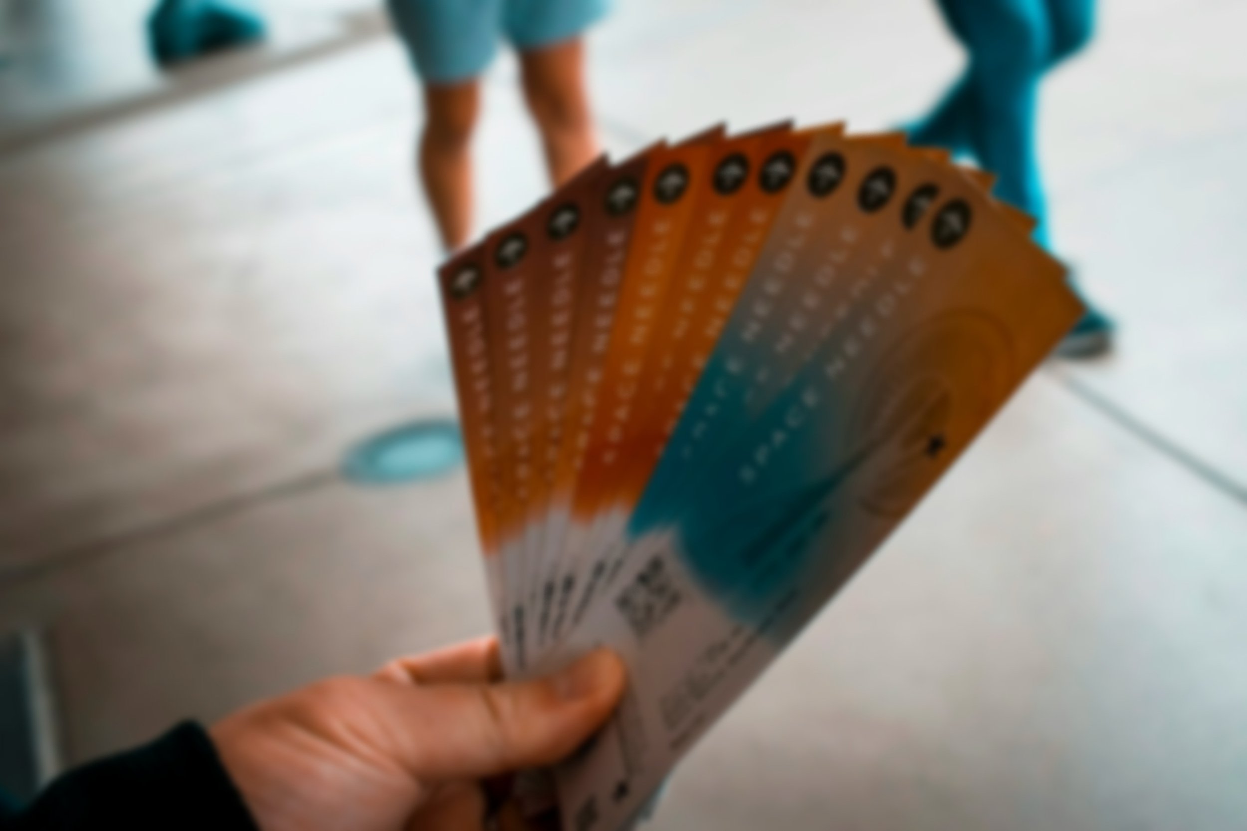 Person holding a fan of orange and blue tickets in a room with a smooth floor.