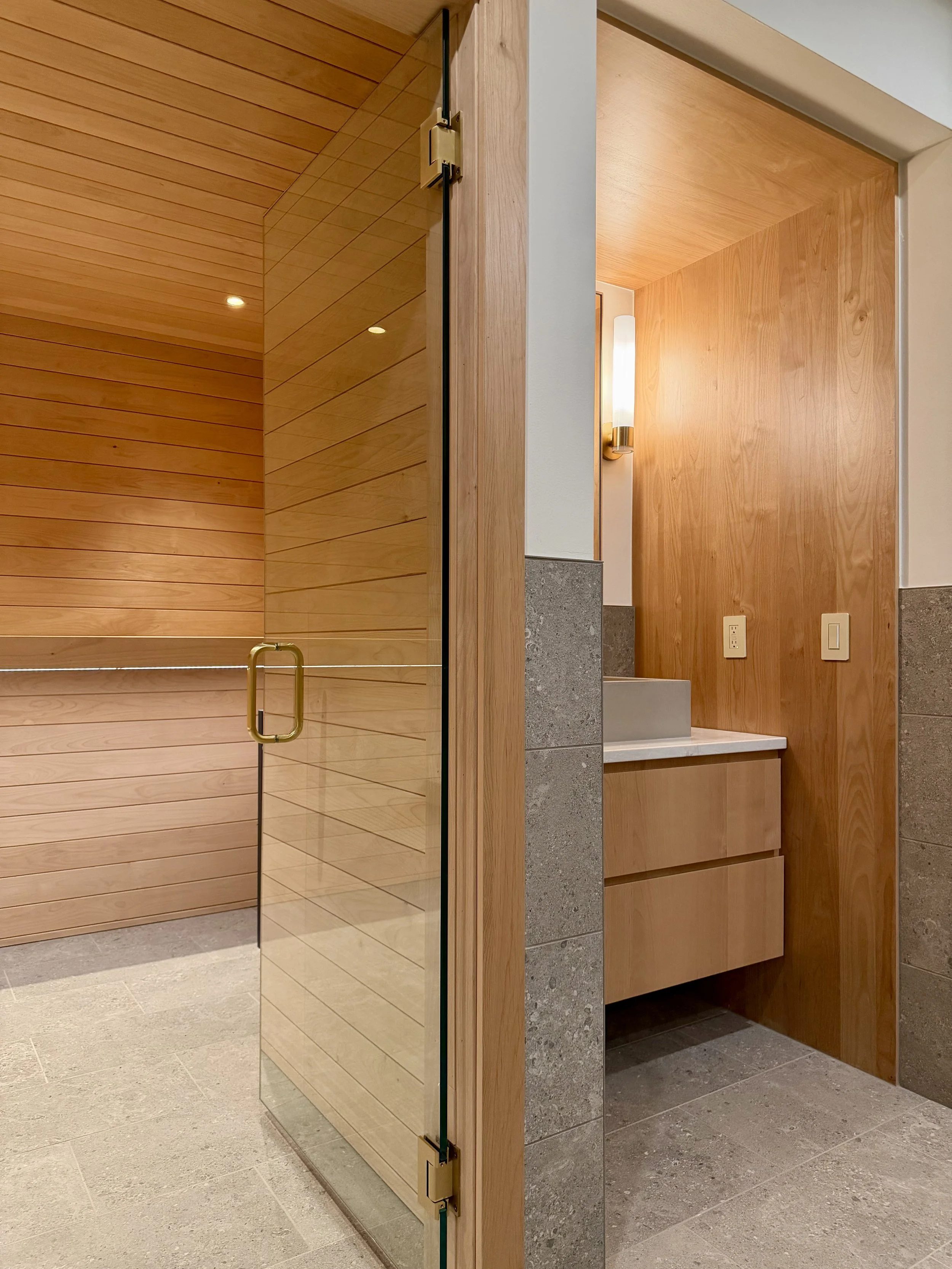 Foreground:

Custom Built Linear Floating Vanity in Uniform Clear Alder Veneer and Alder Hardwoods. Perimeter is Wrapped in 3/4" Edge-banded Alder Plywood Finished with Centurion 2K Polyurethane. 

Electrical & Wall Mounter Plumbing Fixtures are Kohl