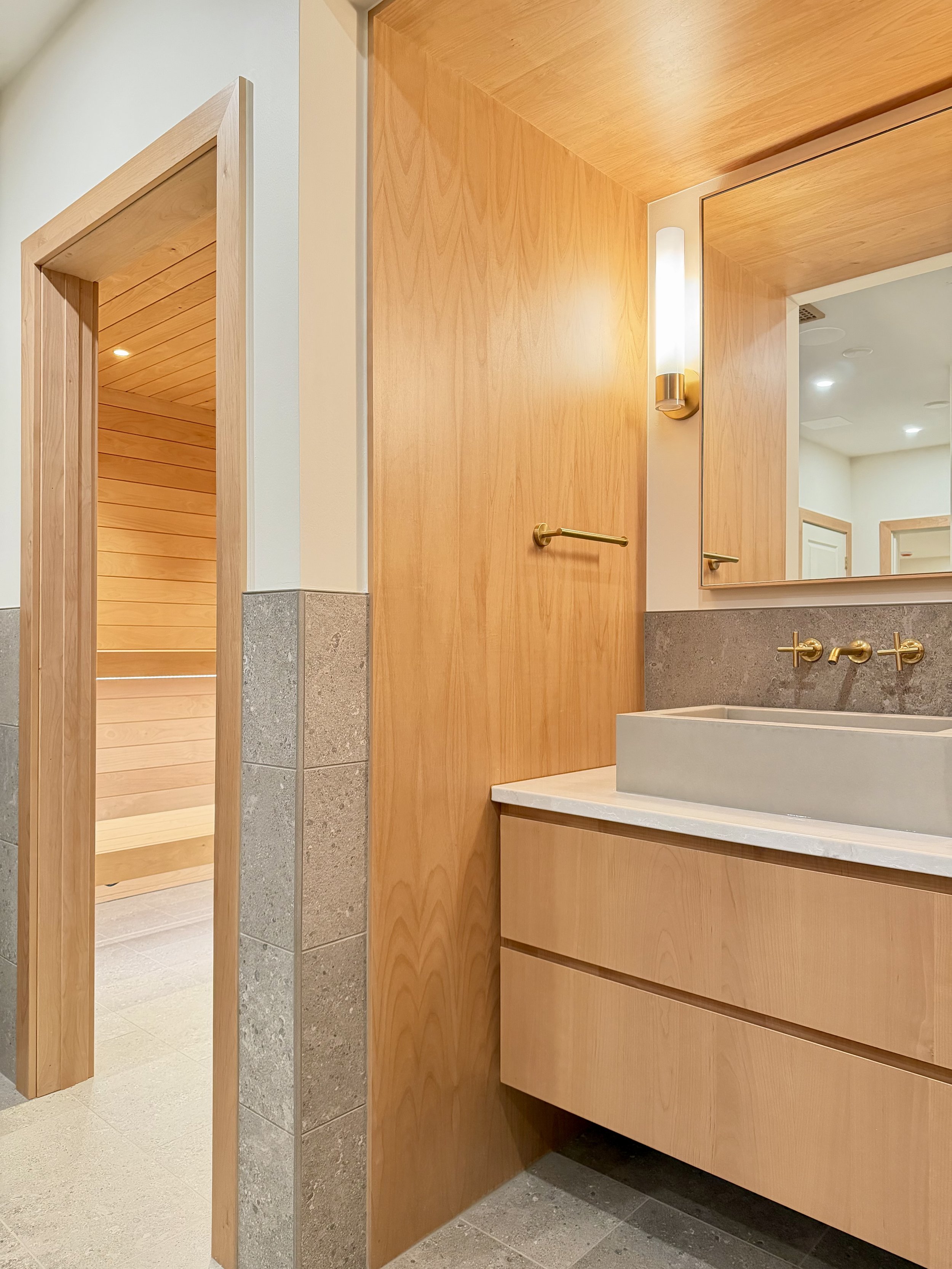 Foreground:

Custom Built Linear Floating Vanity in Uniform Clear Alder Veneer and Alder Hardwoods. Perimeter is Wrapped in 3/4" Edge-banded Alder Plywood Finished with Centurion 2K Polyurethane. 

Electrical & Wall Mounter Plumbing Fixtures are Kohl